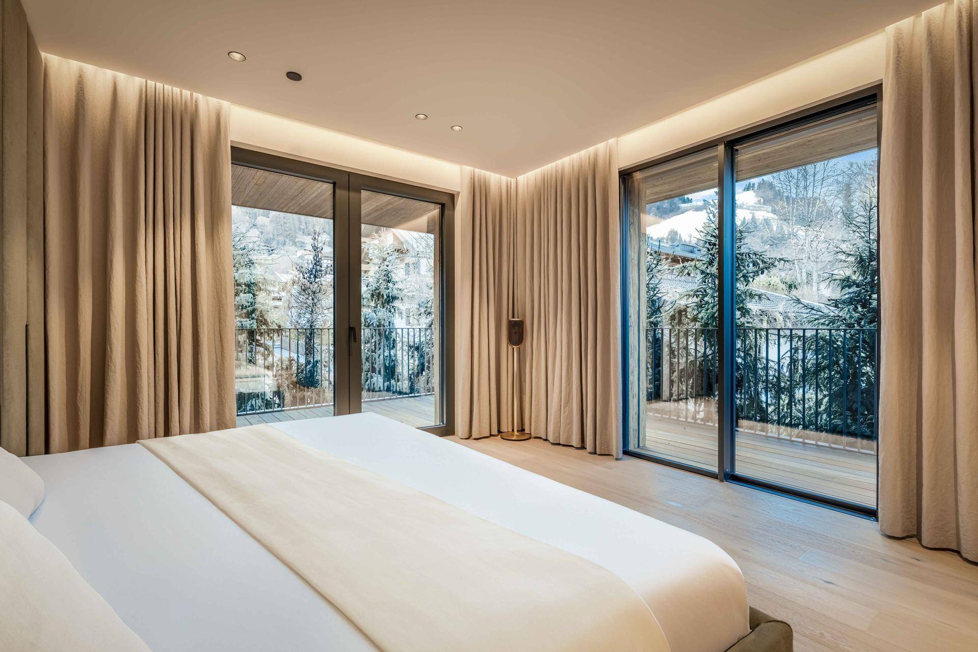 Helles Schlafzimmer mit Holzboden, großen Fenstern und Zugang zu einem Balkon mit Bergblick.