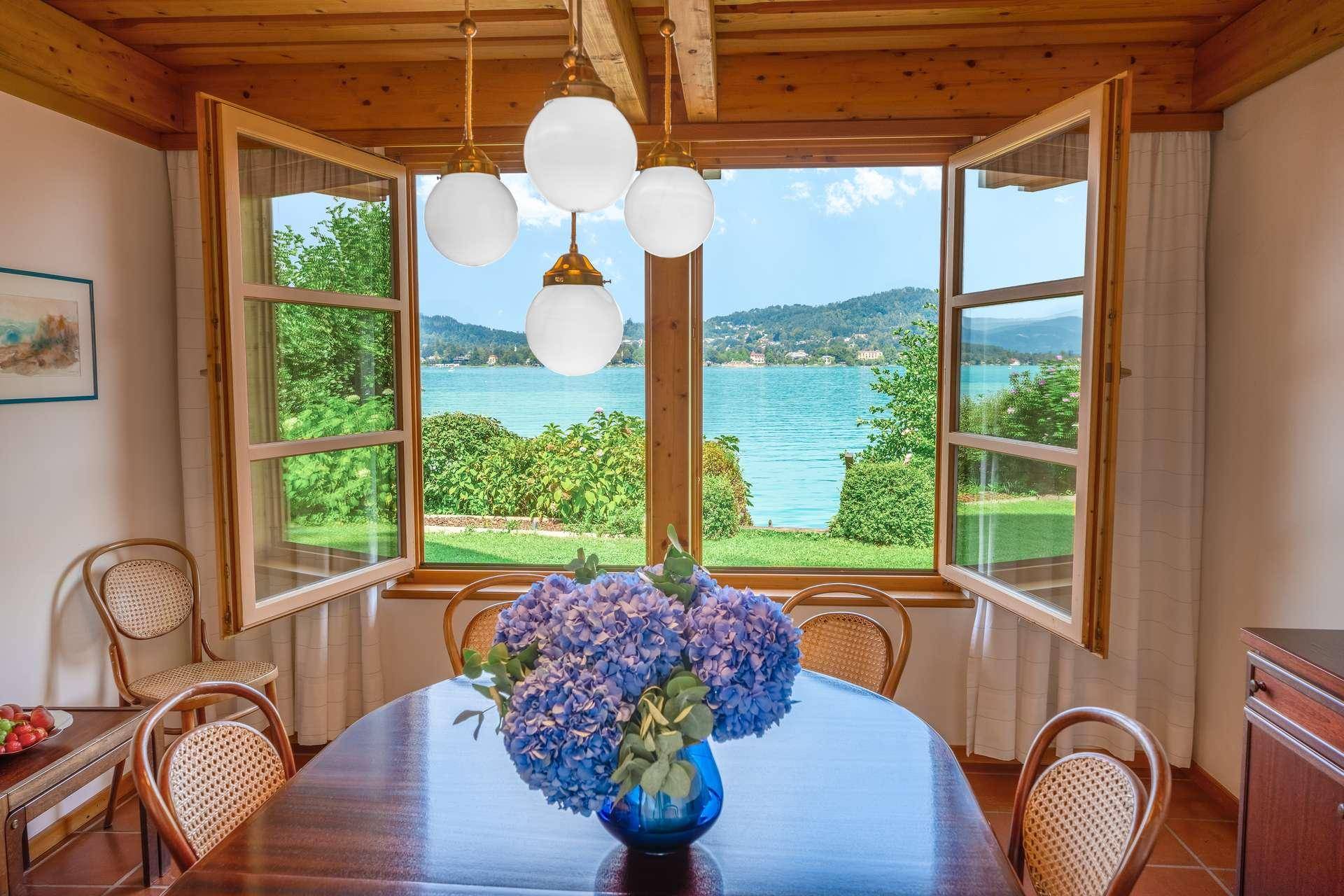 Elegantes Esszimmer mit Holztisch, Korbstühlen und einem großen Fenster mit herrlichem Seeblick.