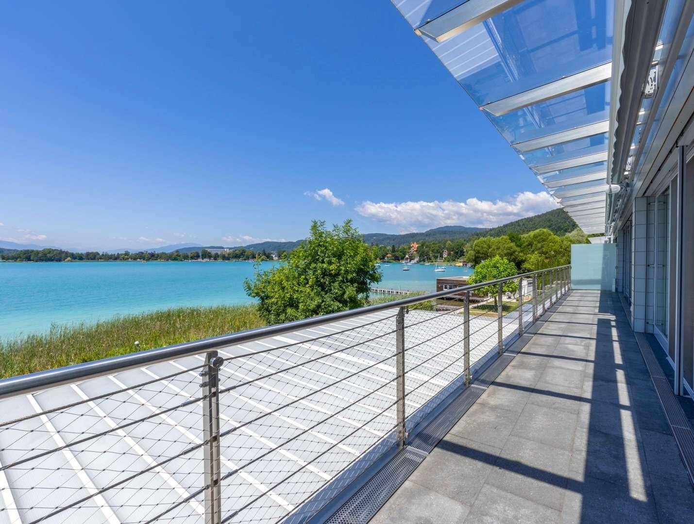 Langer Balkon mit Glasüberdachung und Edelstahlgeländer, der einen weiten Blick über den See bietet.