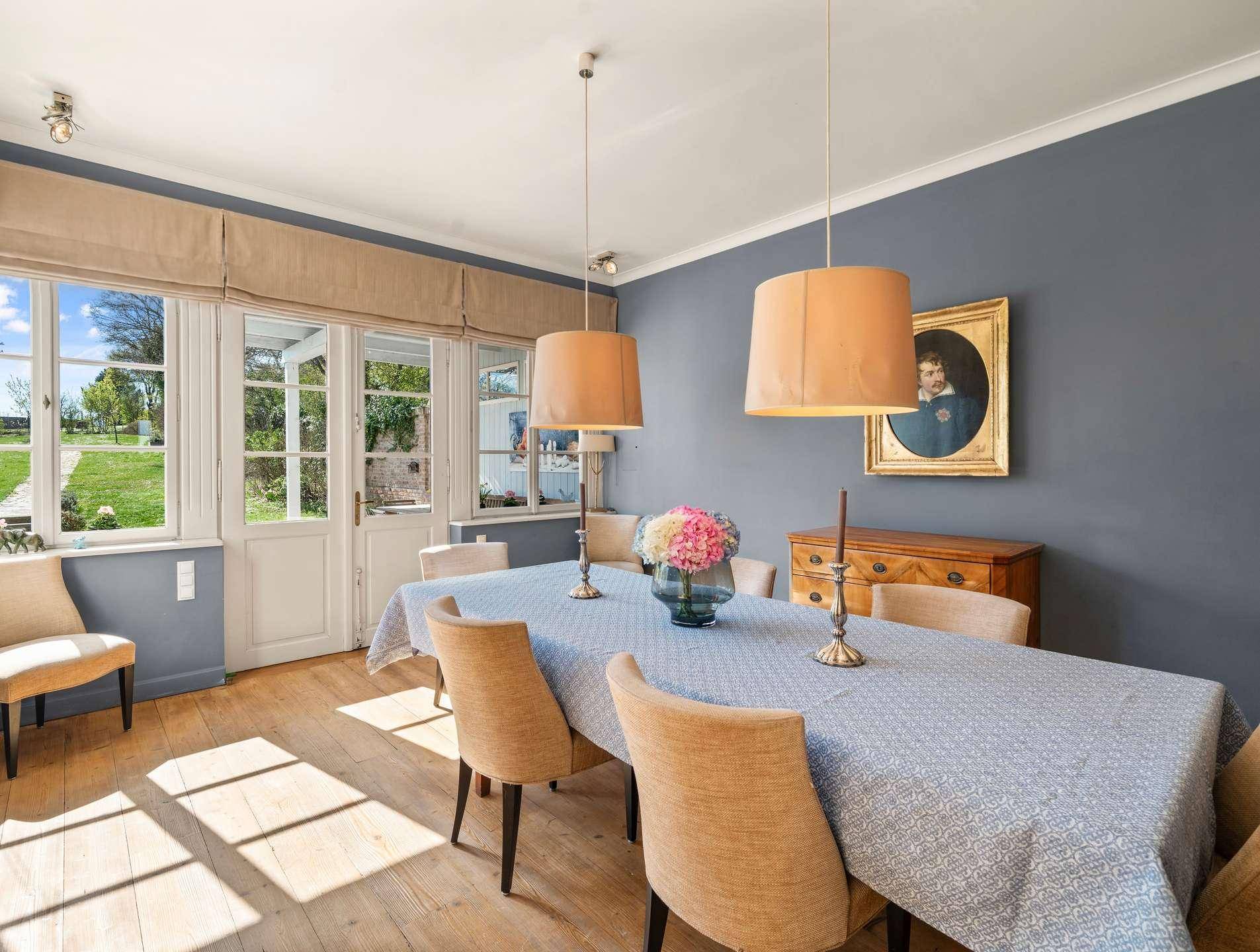 Elegantes Esszimmer mit blau gestrichenen Wänden, großem Esstisch und Zugang zum Außenbereich.