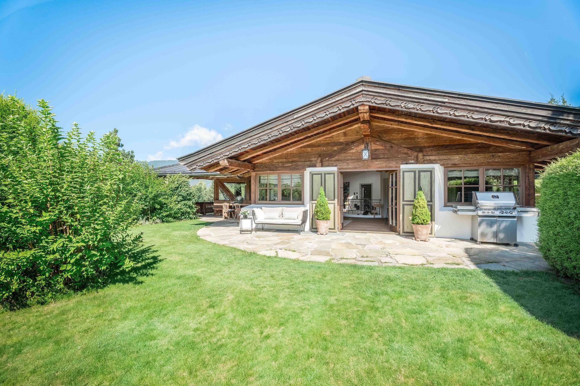 Weitläufige Terrasse mit Grillbereich und Sitzgelegenheiten, umgeben von gepflegtem Rasen und Sträuchern.