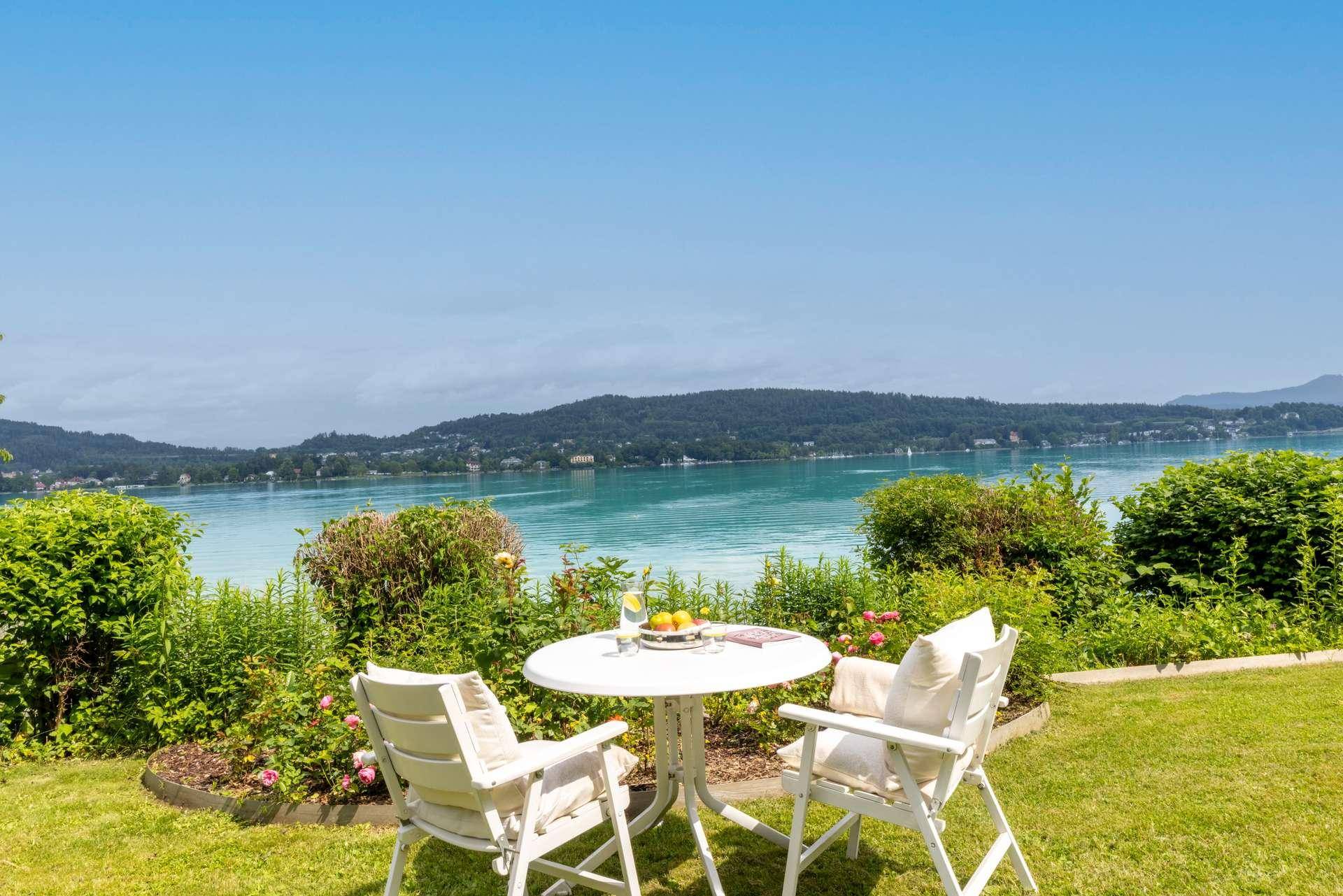 Gemütlicher Sitzbereich im Garten mit weißem Tisch und Stühlen, mit weitem Blick auf den See und die umliegenden Hügel.