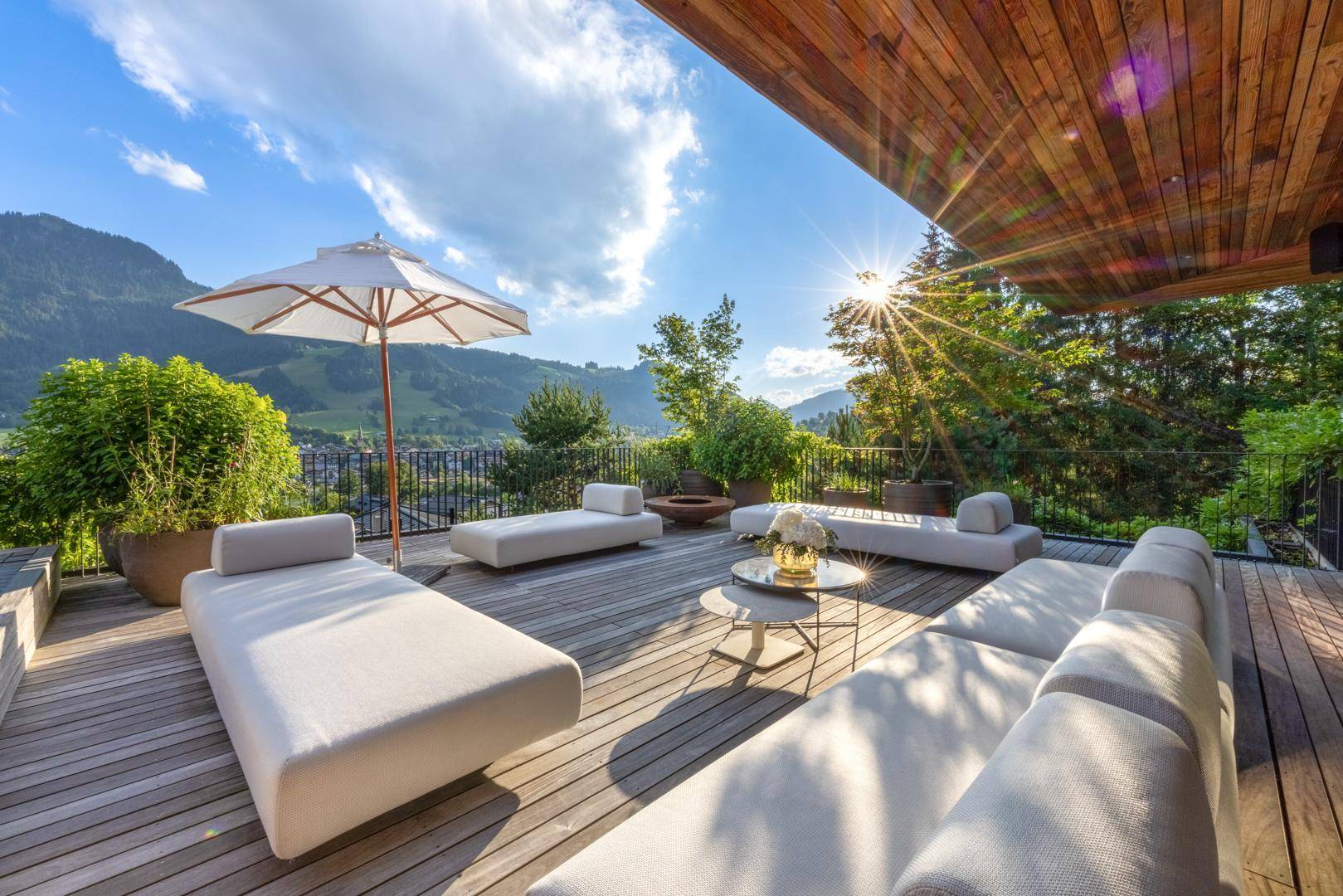 Große Holzterrasse mit bequemen Liegen und Sonnenschirm, ideal zum Entspannen mit Bergblick.