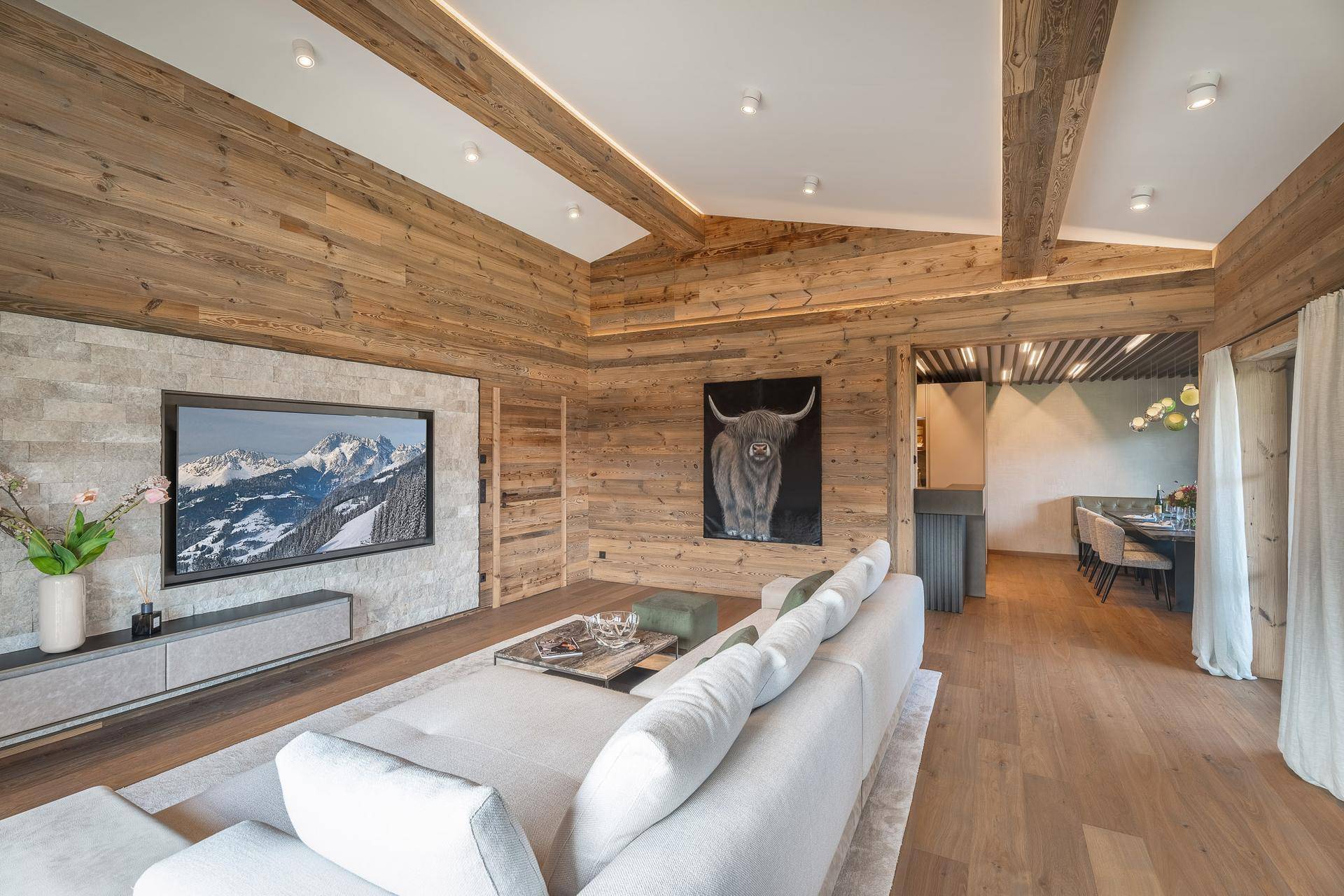 Helles Wohnzimmer mit Holzwänden, integriertem Fernseher und modernem Sofa.