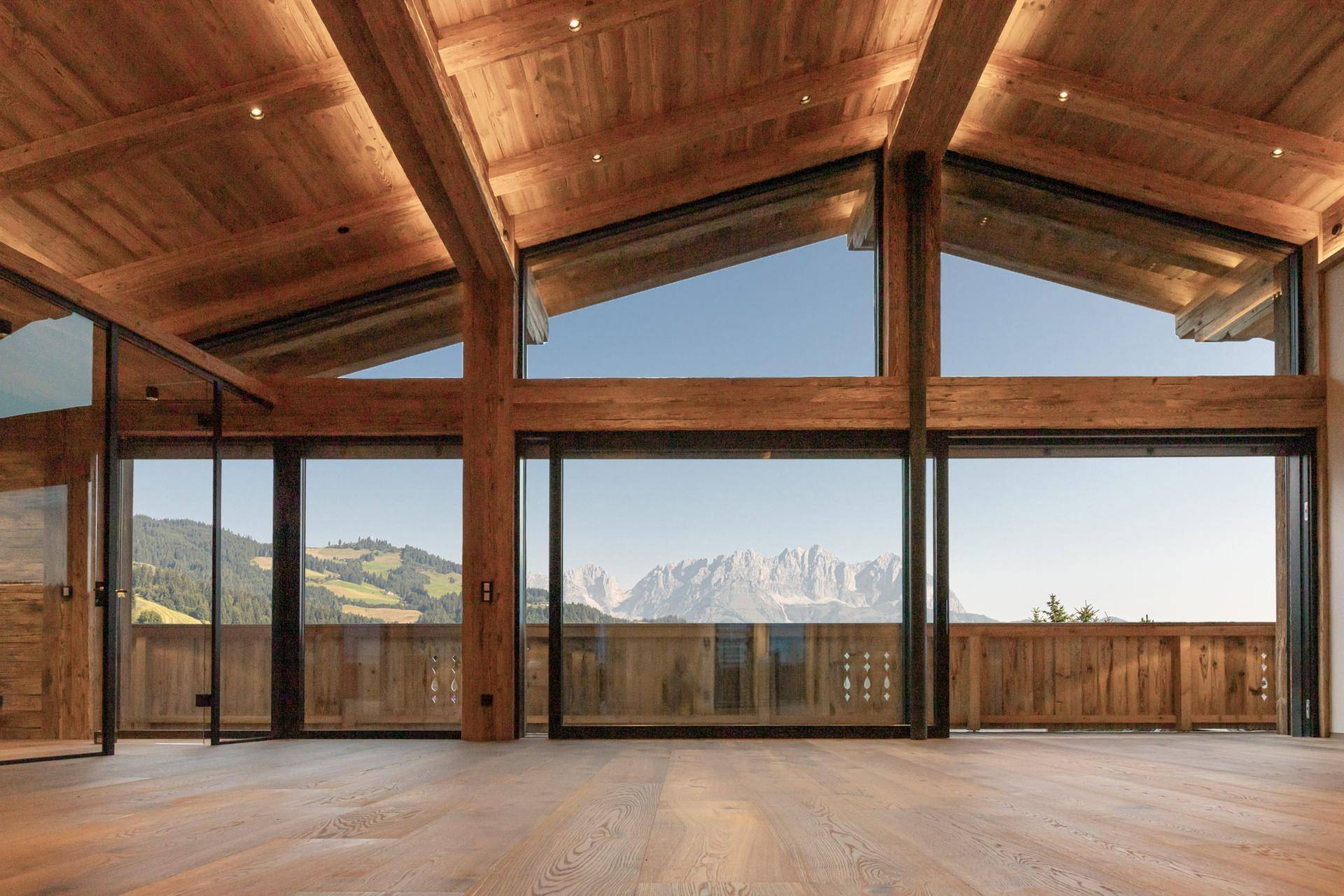 Heller, offener Wohnbereich mit Holzbalken, großen Glasfronten und Panoramablick auf die Berge.