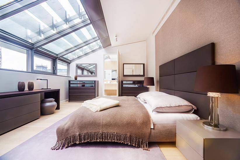 Stilvolles Schlafzimmer mit Doppelbett, dunklen Kommoden und schrägem Glasdach für eine helle Atmosphäre.