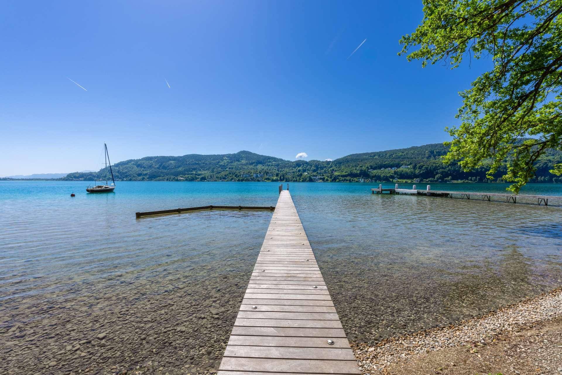 Langer Holzsteg führt in das klare, türkisfarbene Wasser des Sees mit malerischer Bergkulisse.