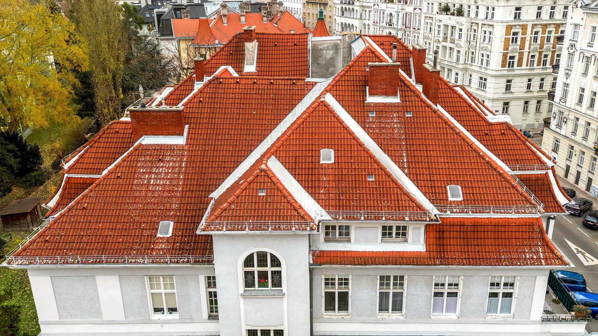Nahaufnahme des komplexen roten Ziegeldachs mit Gaubenfenstern und Schornsteinen eines historischen Gebäudes.