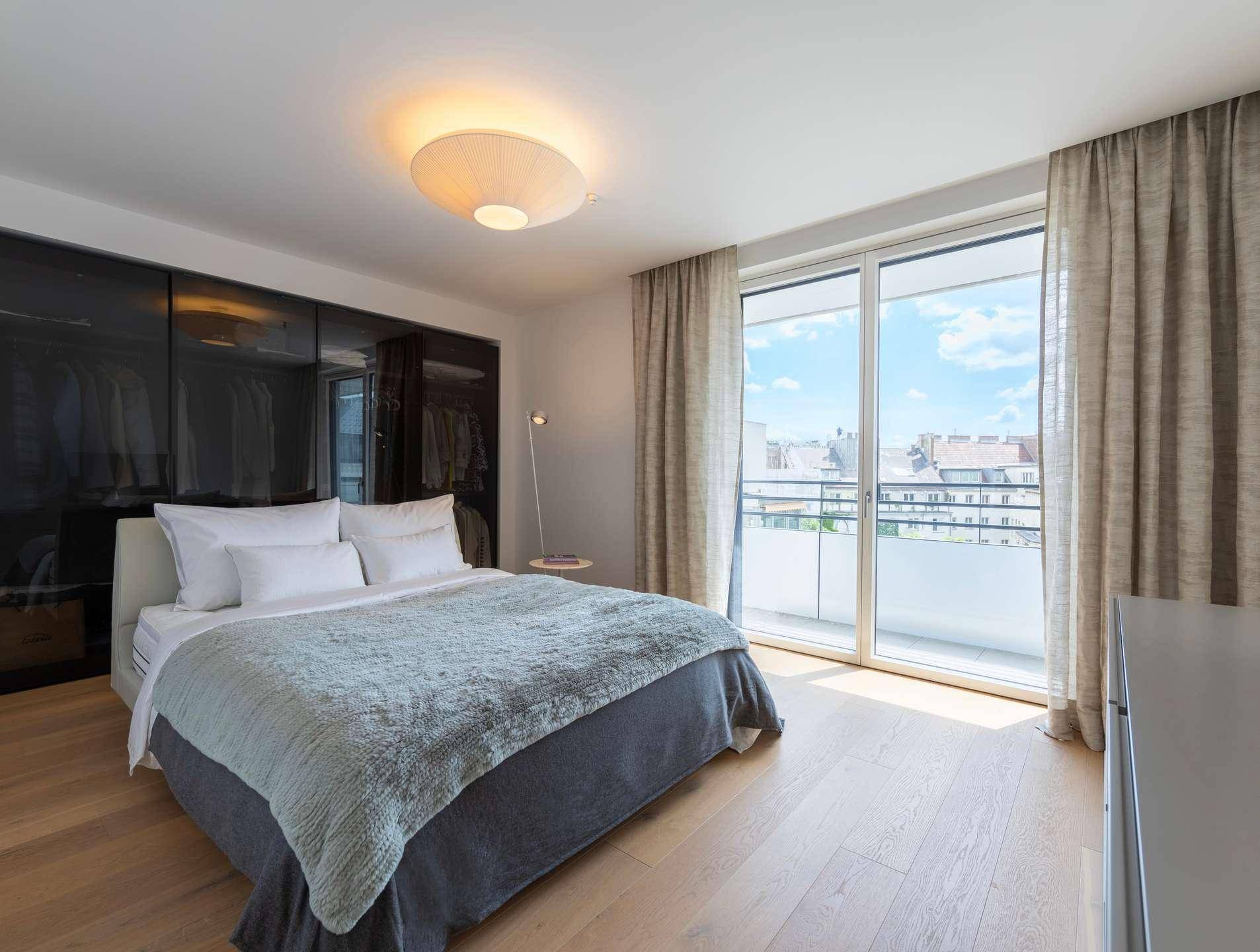 Helles Schlafzimmer mit Holzboden, Einbauschränken und direktem Zugang zu einem Balkon.