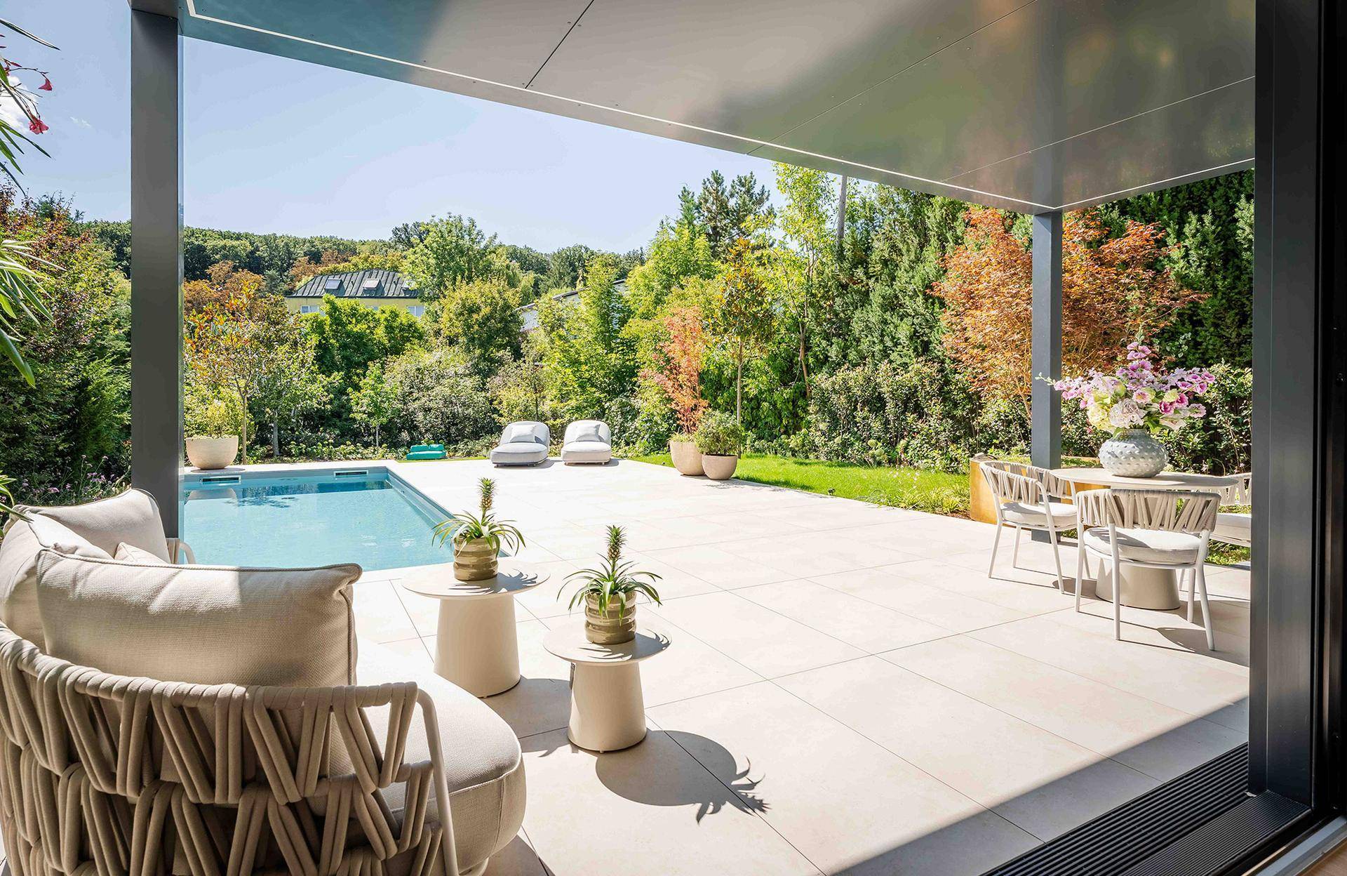 Großzügige überdachte Terrasse mit Lounge-Möbeln, Essbereich und Blick auf den Pool und Garten.
