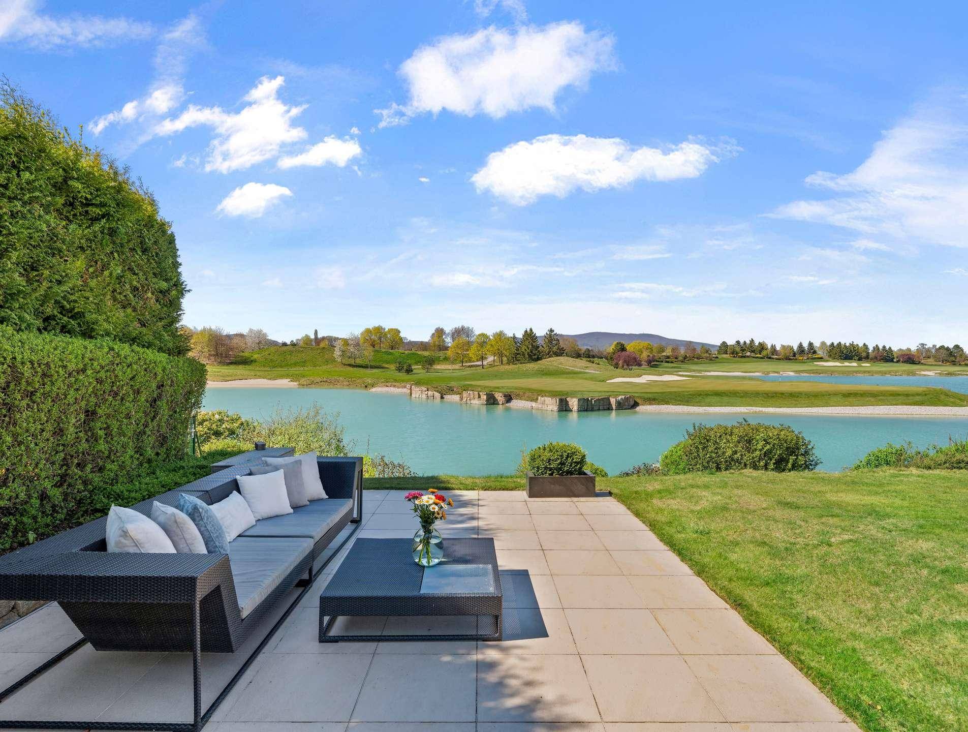 Geräumige Terrasse mit bequemen Lounge-Möbeln und direktem Blick auf den See und Golfplatz.