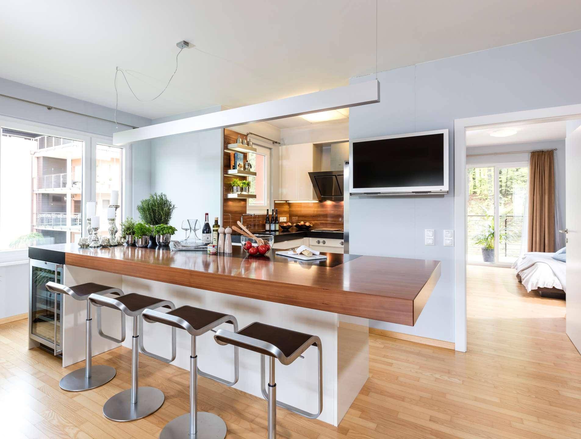 Moderne Küche mit Holztheke, Barhockern und integrierten Geräten, offen zum Wohnbereich und Schlafzimmer.
