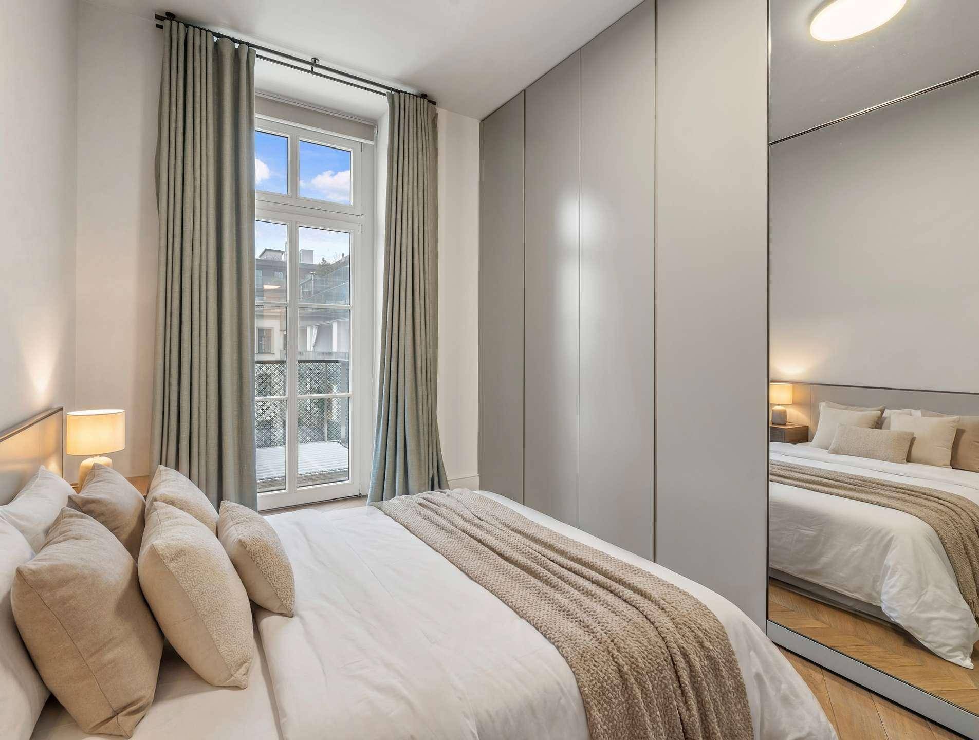 Helles Schlafzimmer mit großem Fenster, Einbauschränken und bequemen Bett in neutralen Farben.