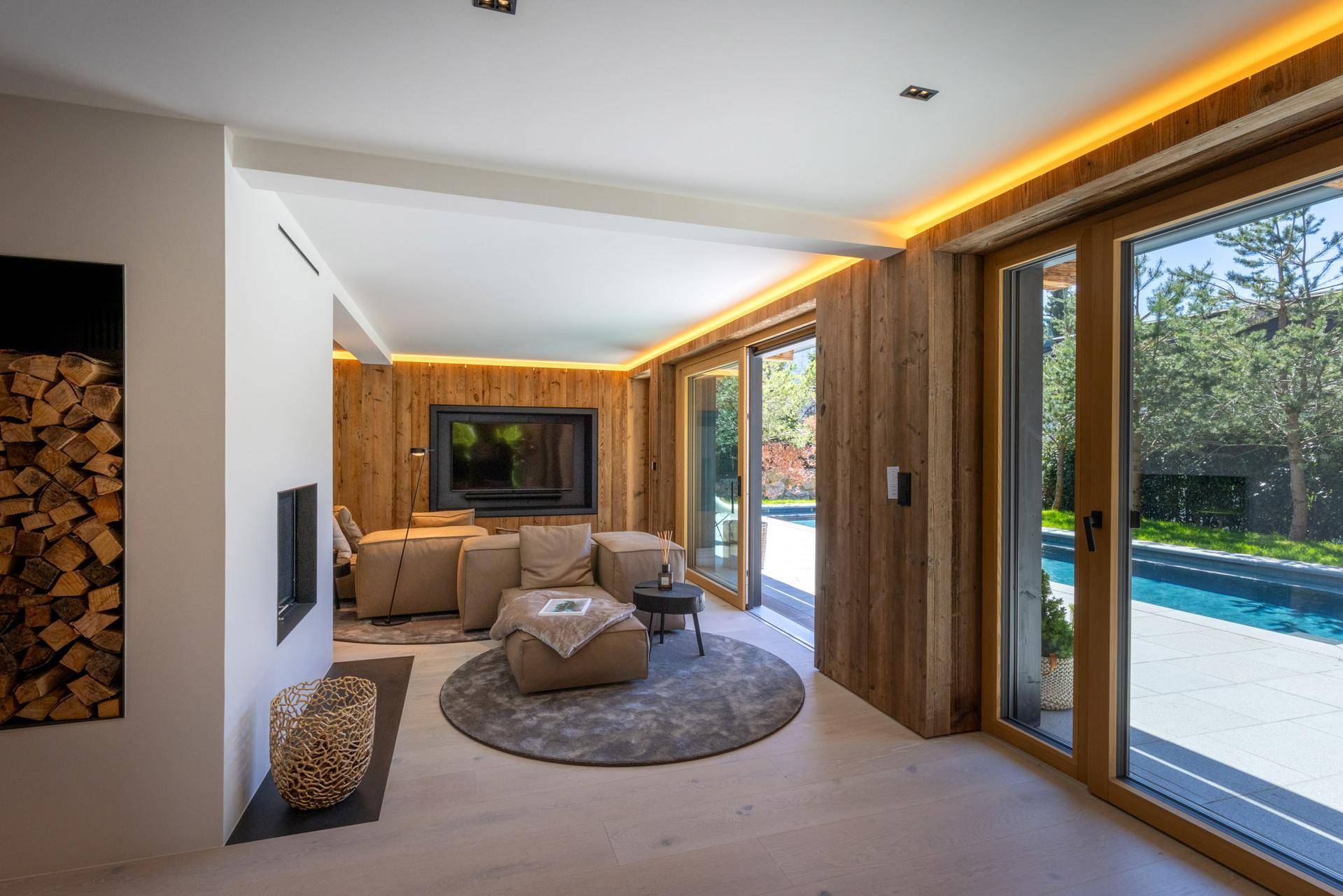Gemütliches Wohnzimmer mit Holzwänden, Kamin und direktem Zugang zum Außenpool.