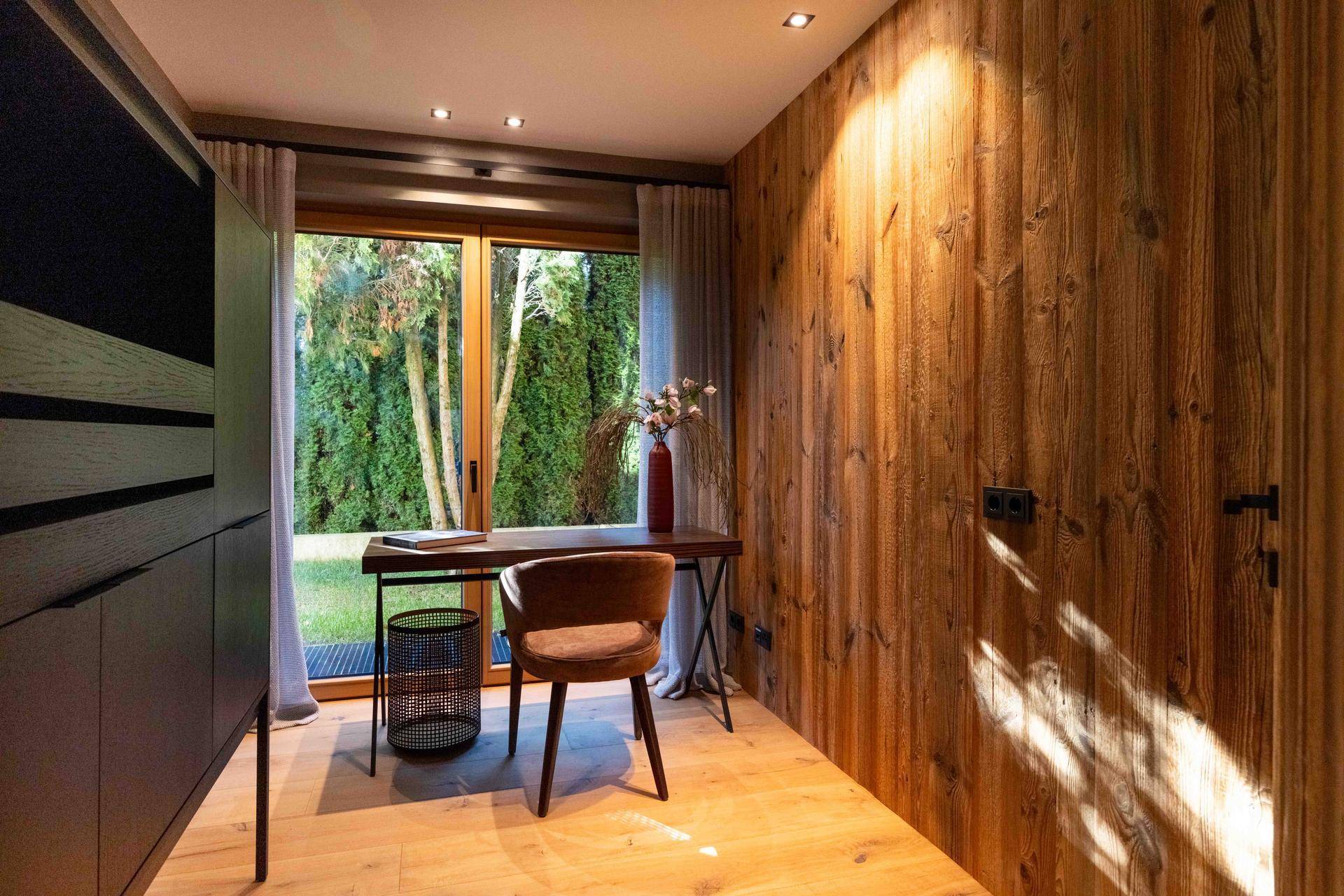 Helles Arbeitszimmer mit Holzwänden, Schreibtisch und Blick in den Garten.