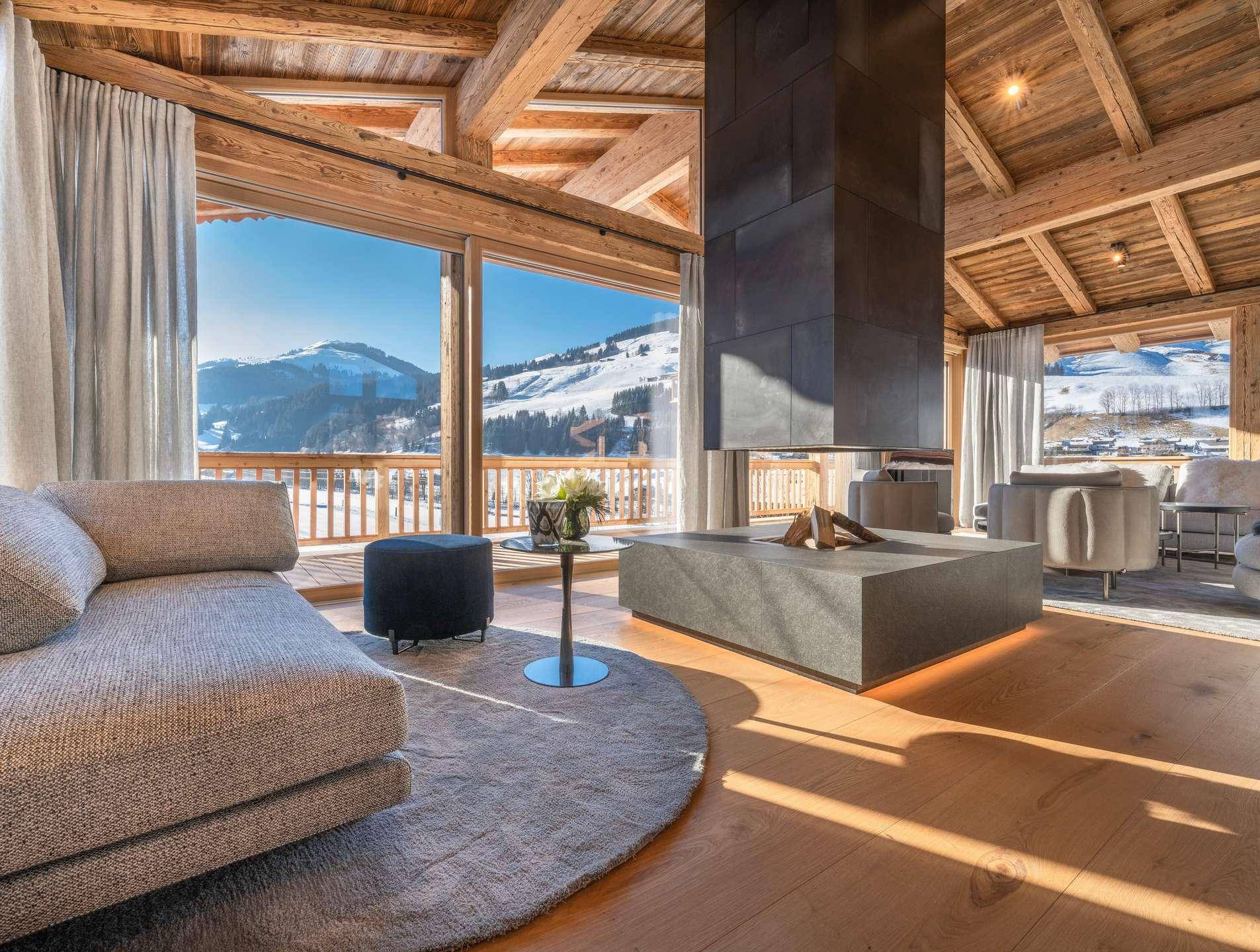 Heller Wohnbereich mit modernem Kamin und großen Glasfronten, die einen weiten Blick auf die Berge bieten.