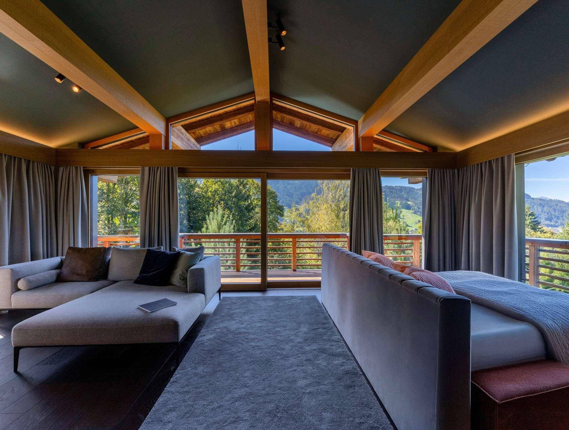Geräumiges Schlafzimmer mit Holzbalken, großen Fenstern und Zugang zu einem Balkon mit Bergblick.