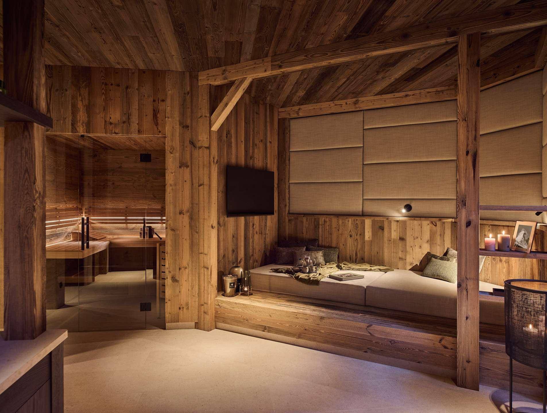 Entspannungsbereich im alpinen Stil mit Holzvertäfelung, bequemer Liegefläche und angrenzender Sauna.