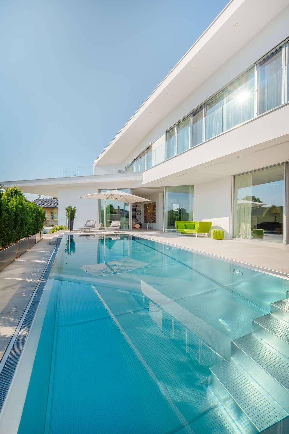 Langer, eleganter Poolbereich mit moderner Architektur und großen Glasfronten des Hauses.