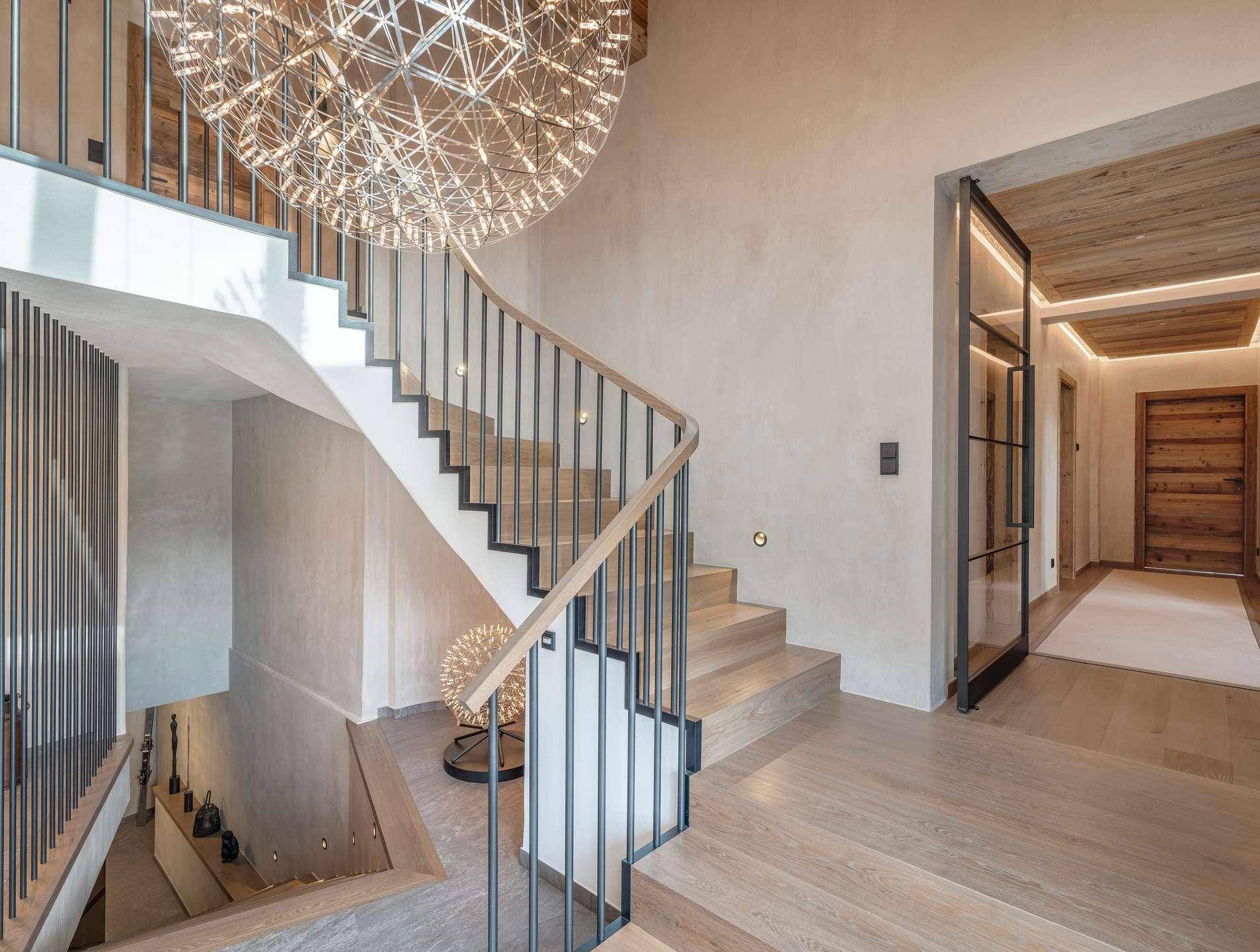 Elegantes Treppenhaus mit moderner Beleuchtung, Holzstufen und Glas-Holz-Türen.