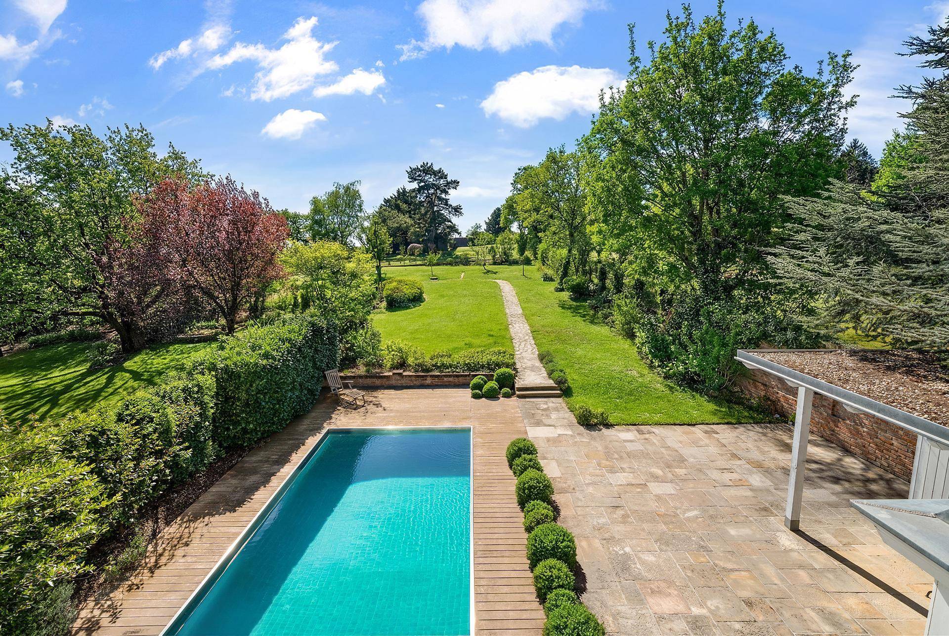 Weitläufiger Gartenbereich mit Swimmingpool, gepflegtem Rasen und altem Baumbestand.