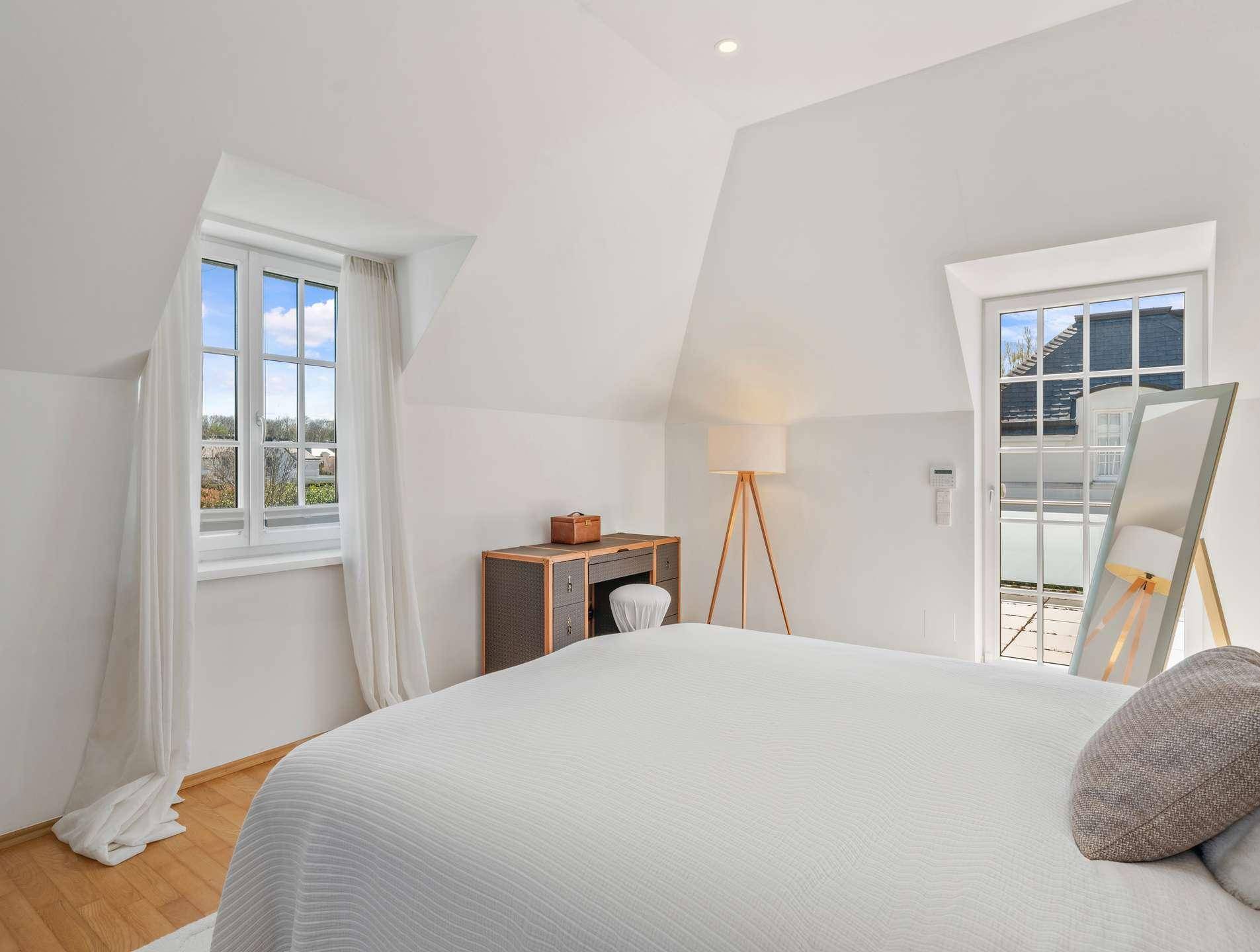 Helles Schlafzimmer im Dachgeschoss mit Holzboden, großen Fenstern und minimalistischer Einrichtung.