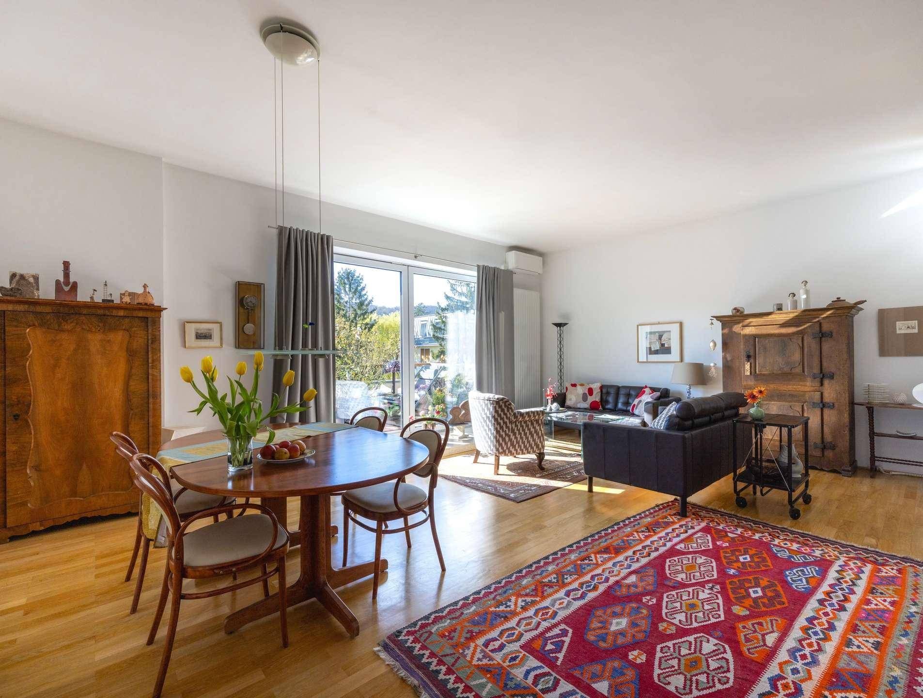 Gemütlicher Wohn-Essbereich mit Holzboden, traditionellen Möbeln und Zugang zum Balkon.
