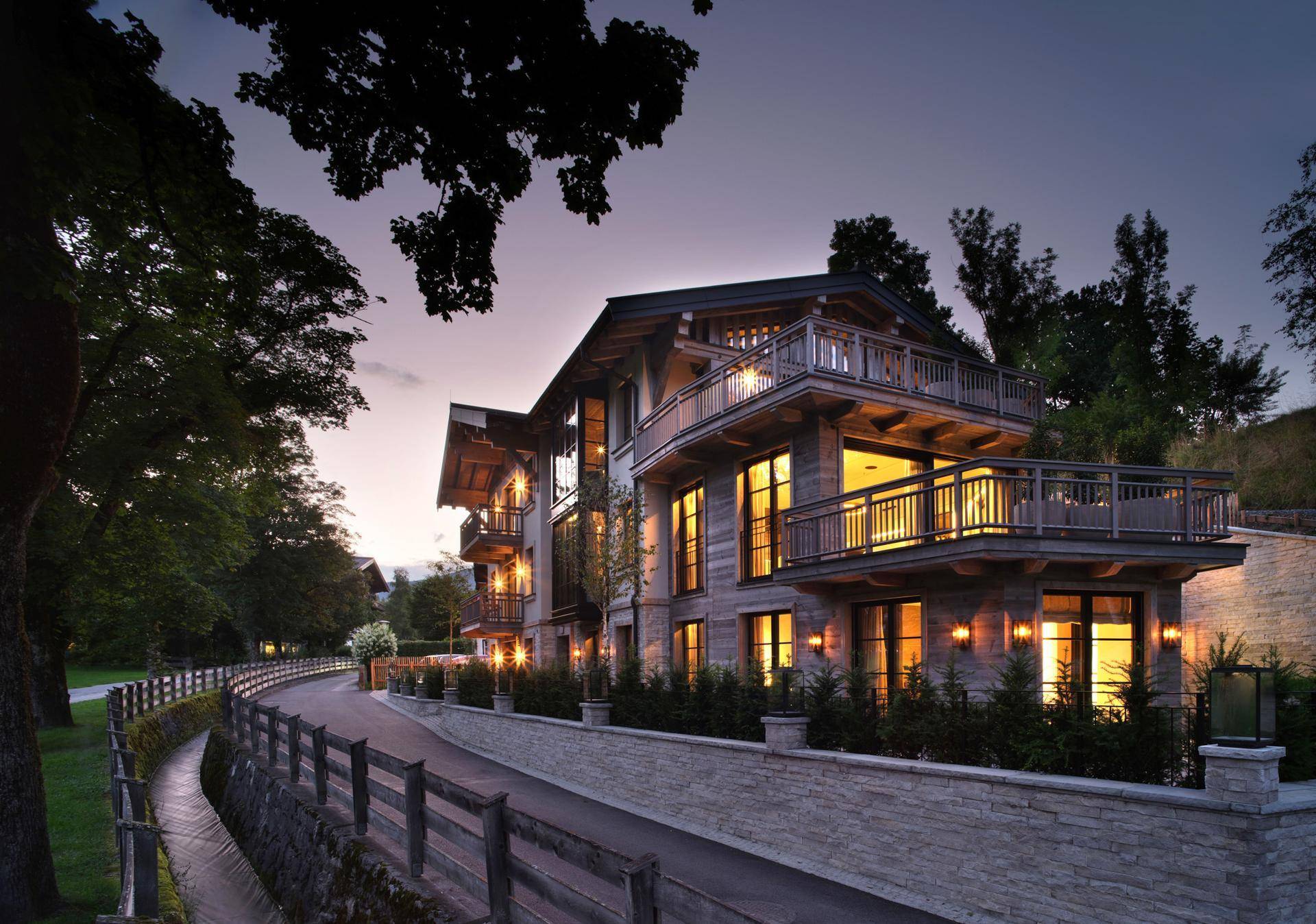 Elegantes Gebäude im Chalet-Stil bei Sonnenuntergang mit beleuchteten Balkonen und Fassade.
