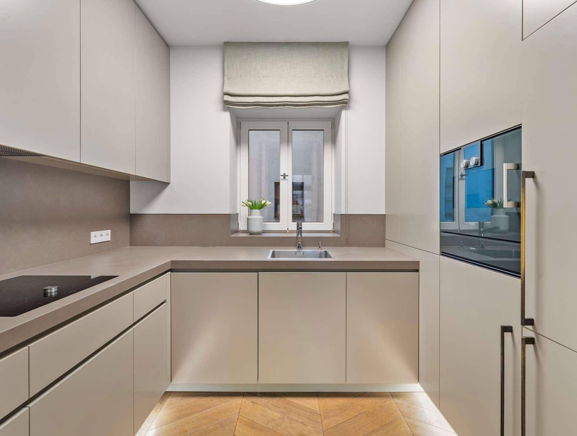 Moderne, kompakte Küche mit beigen Schränken, integrierten Geräten und Fenster über der Spüle.