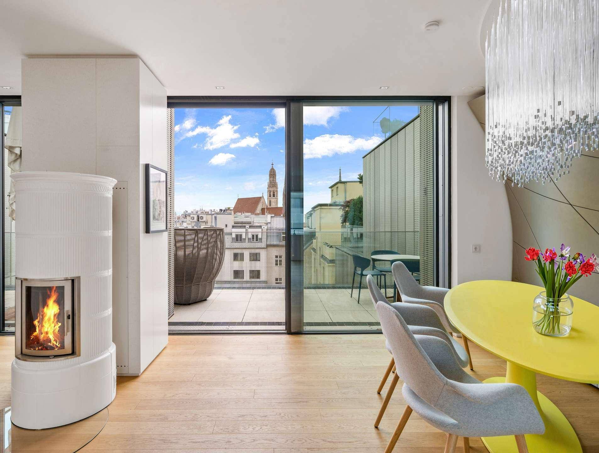 Heller Wohn- und Essbereich mit Kachelofen, Holzboden und Zugang zur Terrasse mit Stadtblick.