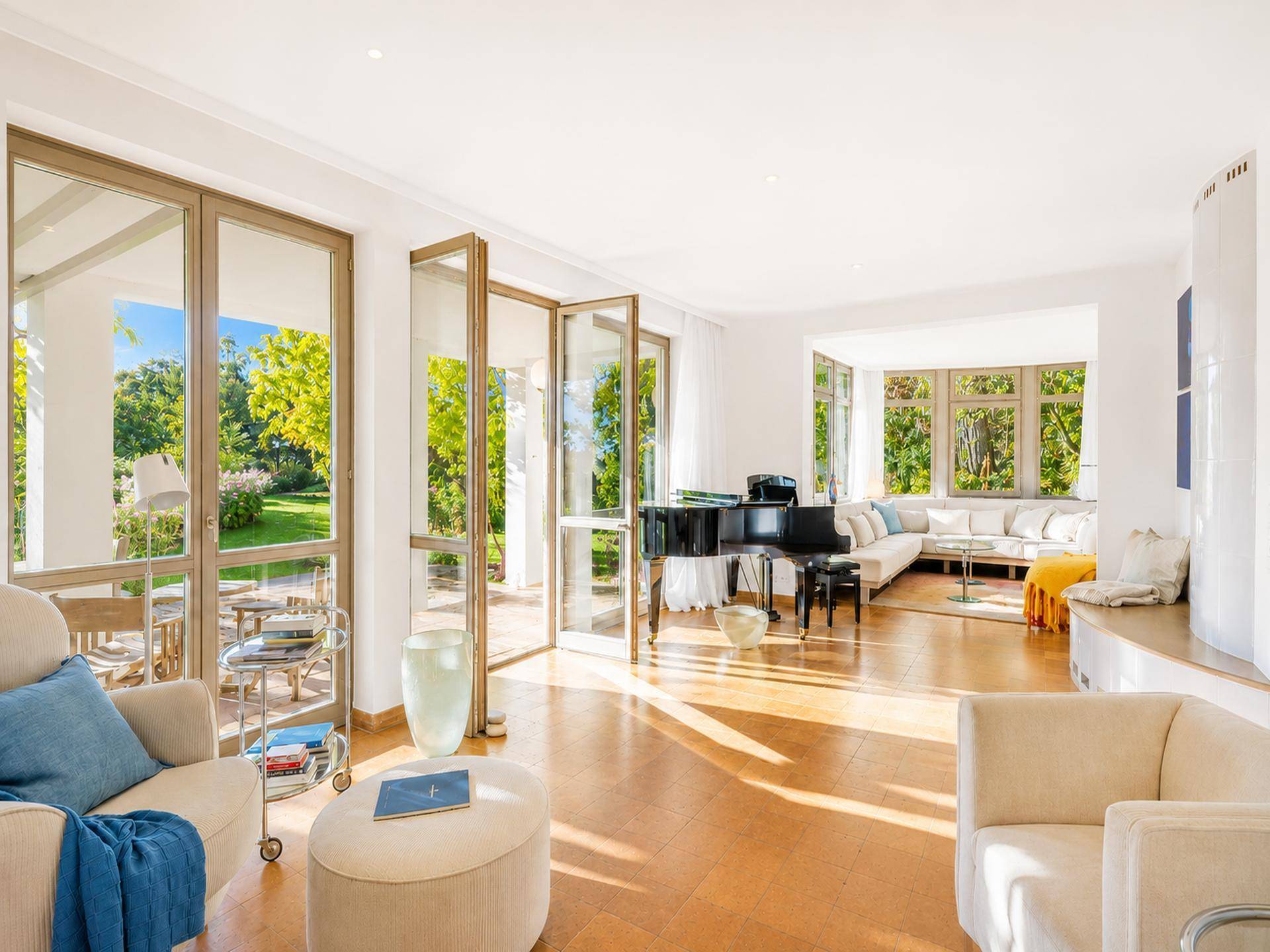 Helles Wohnzimmer mit großen Fenstern, Holzboden, Flügel und Zugang zur Terrasse.
