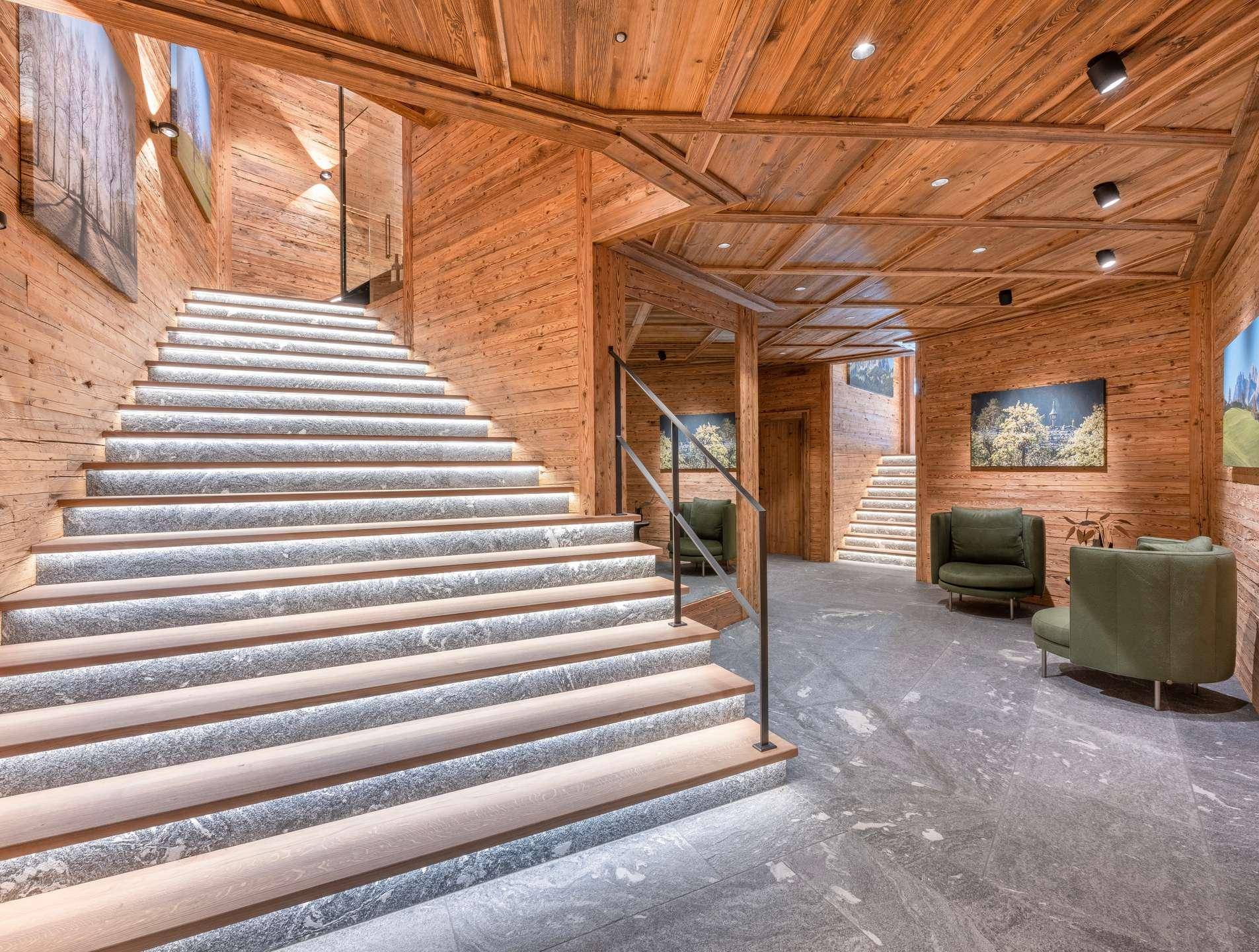 Elegante Eingangshalle mit breiter, beleuchteter Treppe und hochwertigen Holzverkleidungen an Wänden und Decke.