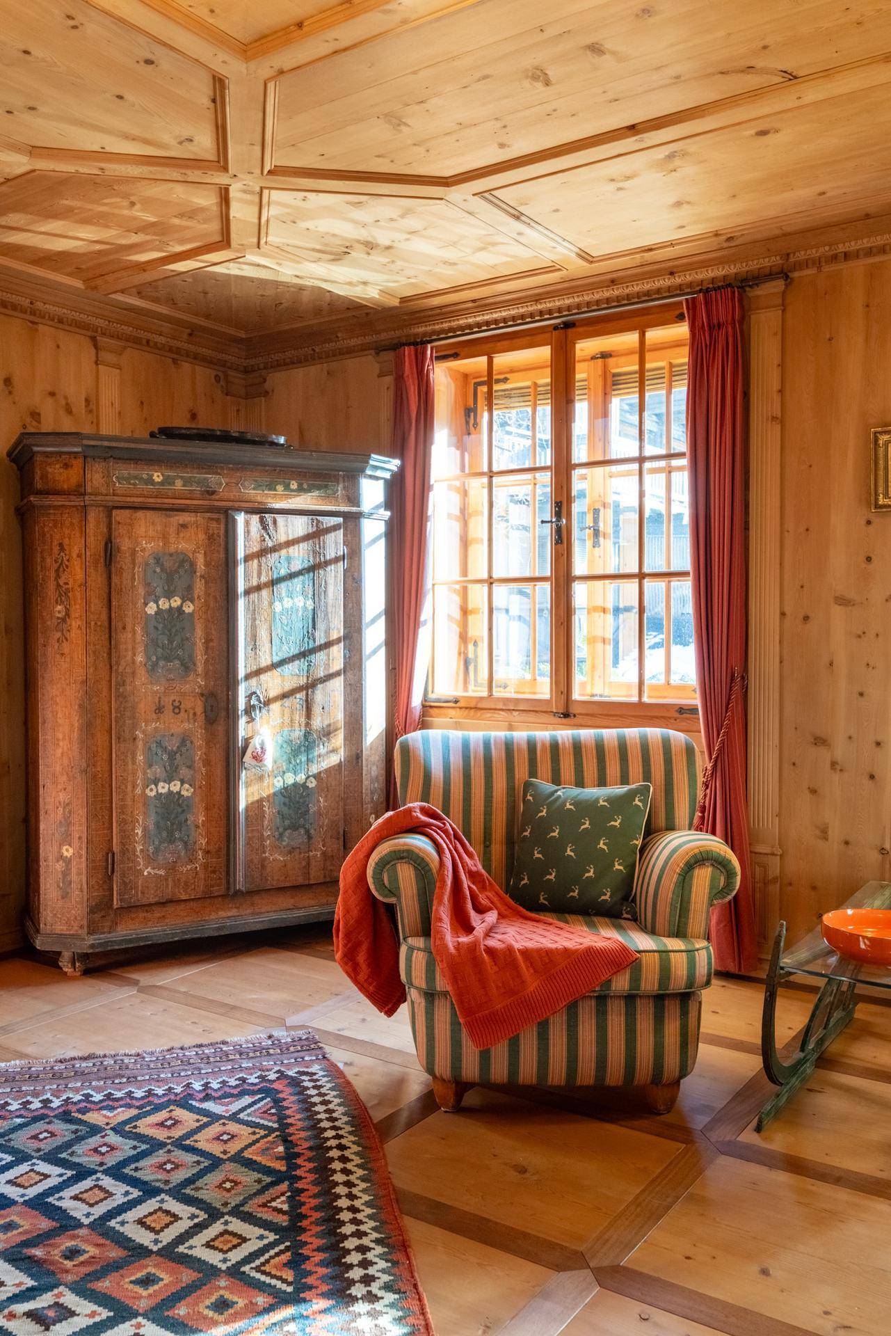 Detailansicht eines traditionellen Schranks und Sessels in einem holzgetäfelten Wohnzimmer.