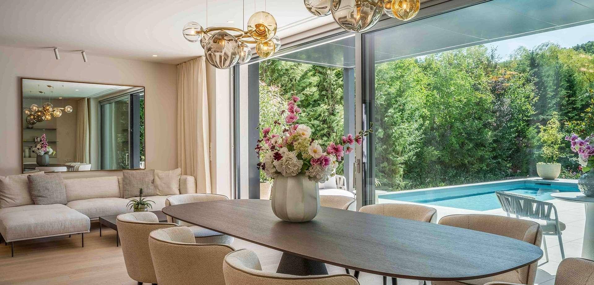 Lichtdurchfluteter Wohn-Essbereich mit großen Glasfronten, modernem Interieur und direktem Zugang zum Poolbereich.