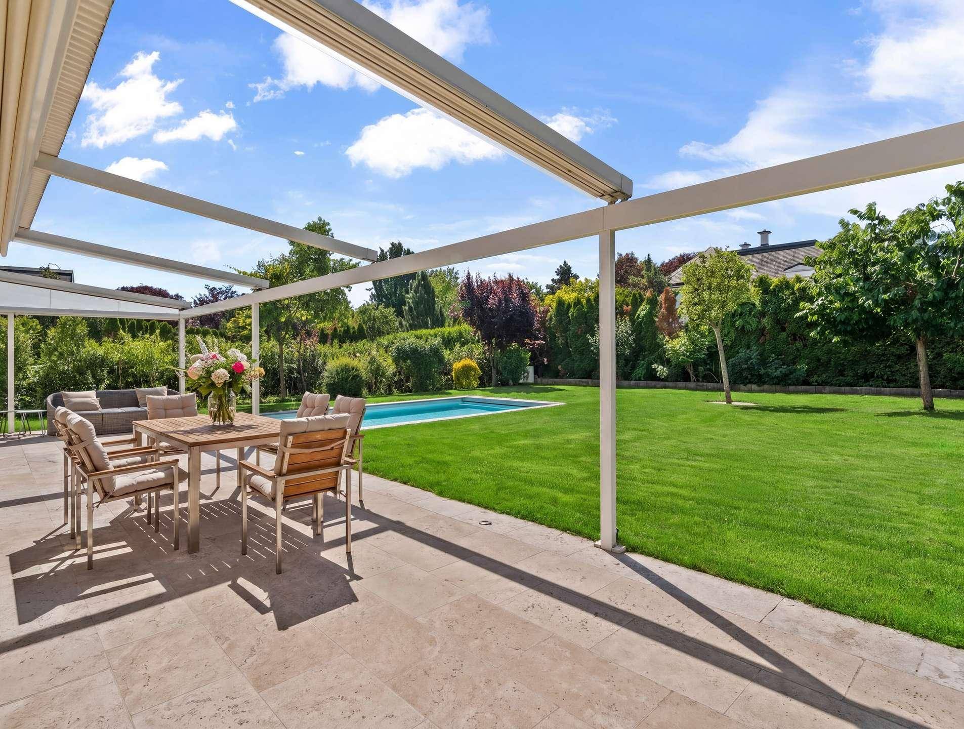 Großzügige Terrasse mit Essbereich im Freien und Blick auf den Pool und den Garten.