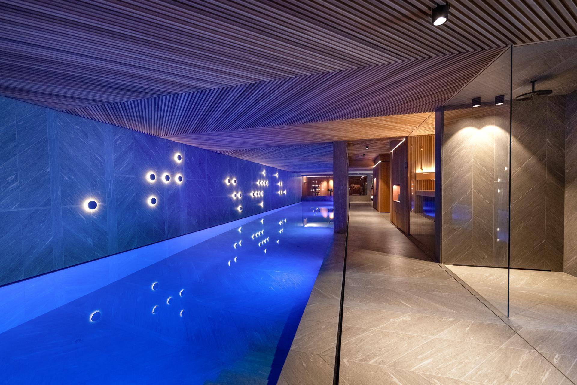 Exklusiver Innenpoolbereich mit stimmungsvoller Beleuchtung, Holzdecke und angrenzendem Wellnessbereich.