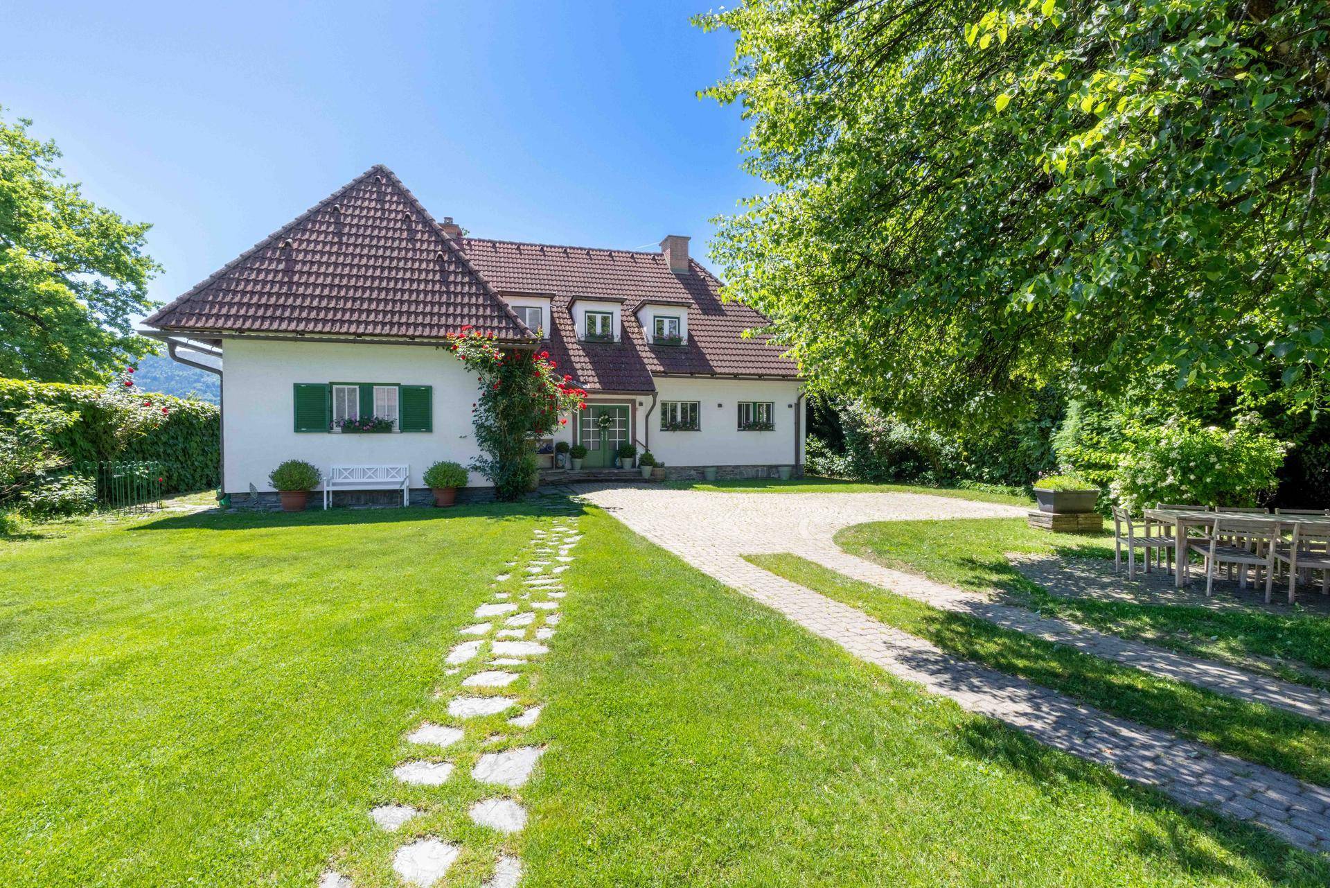 Attraktives Landhaus mit großem Vorgarten, gepflegtem Rasen und geschwungener Auffahrt unter blauem Himmel.