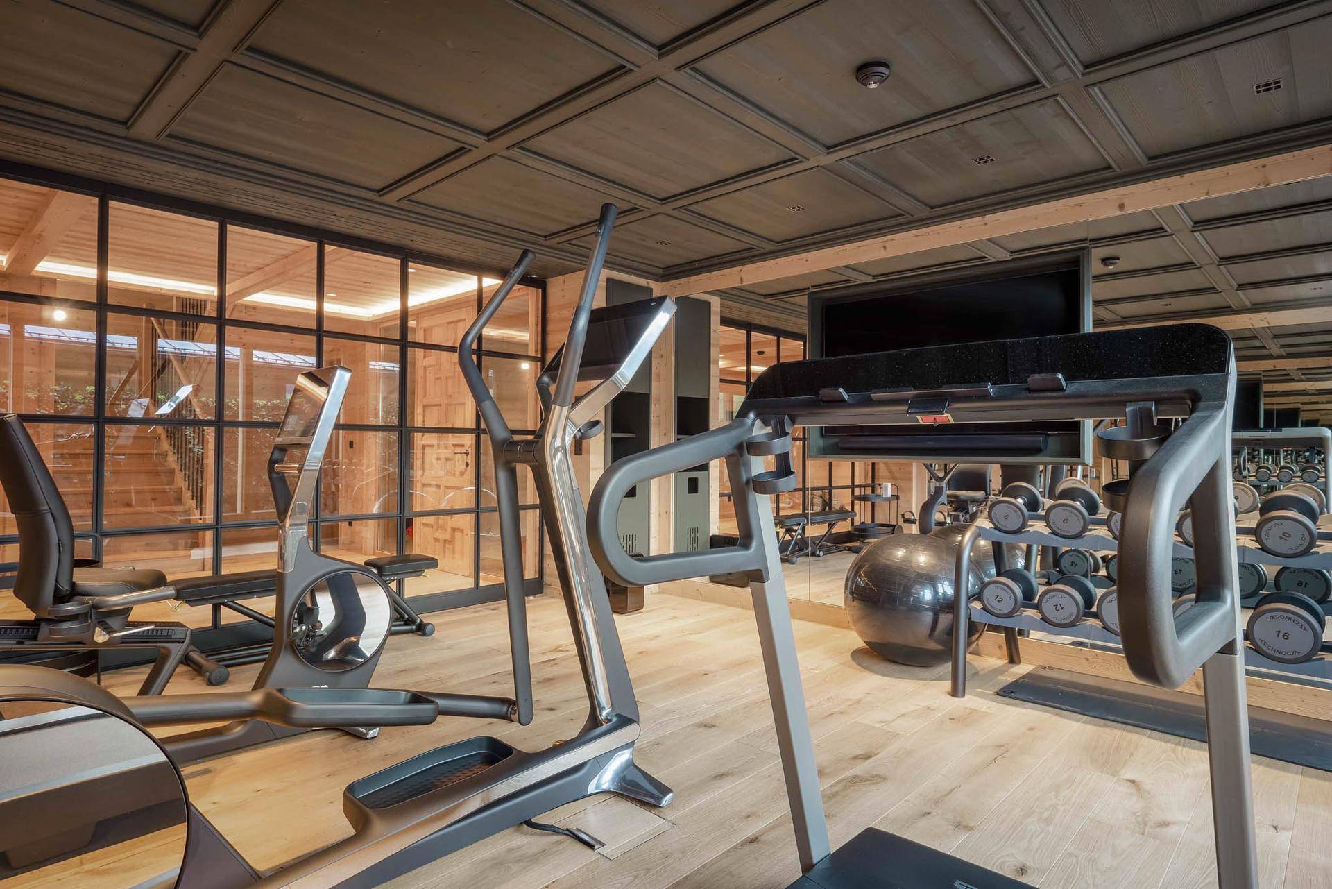 Moderner Fitnessraum mit verschiedenen Trainingsgeräten und Holzboden.