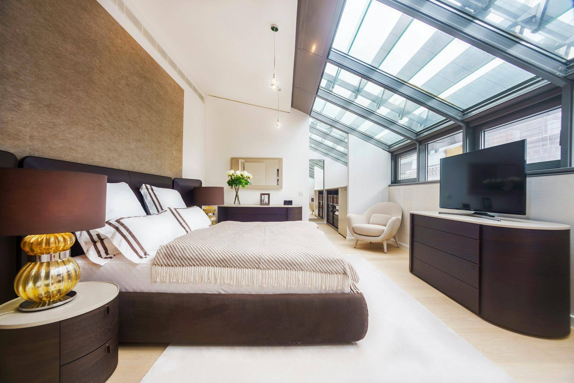 Elegantes Schlafzimmer mit großem Bett, modernen Möbeln und schrägem Glasdach für viel Helligkeit.