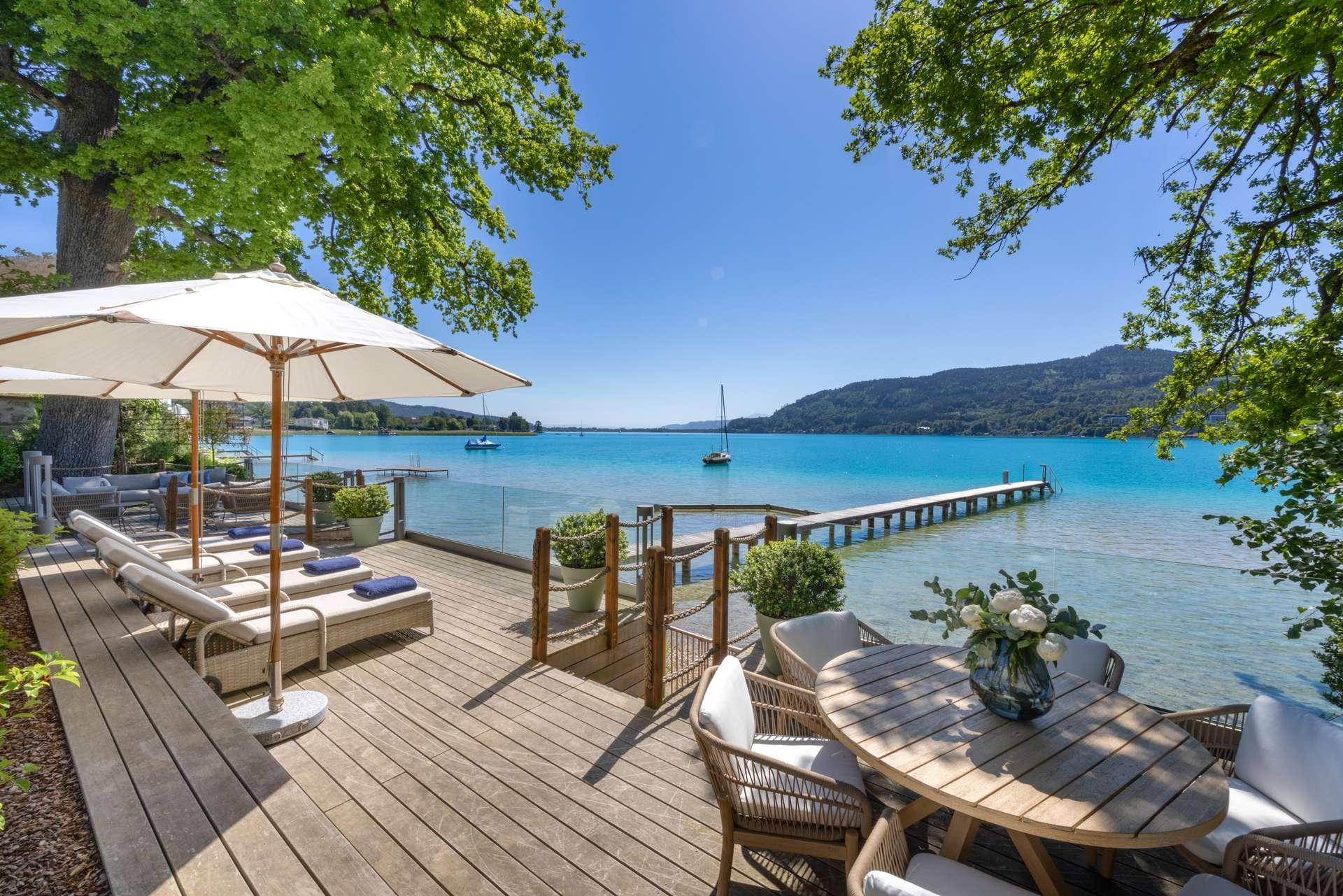 Sonnige Holzterrasse mit Essbereich, Liegestühlen und direktem Zugang zum Seeufer.