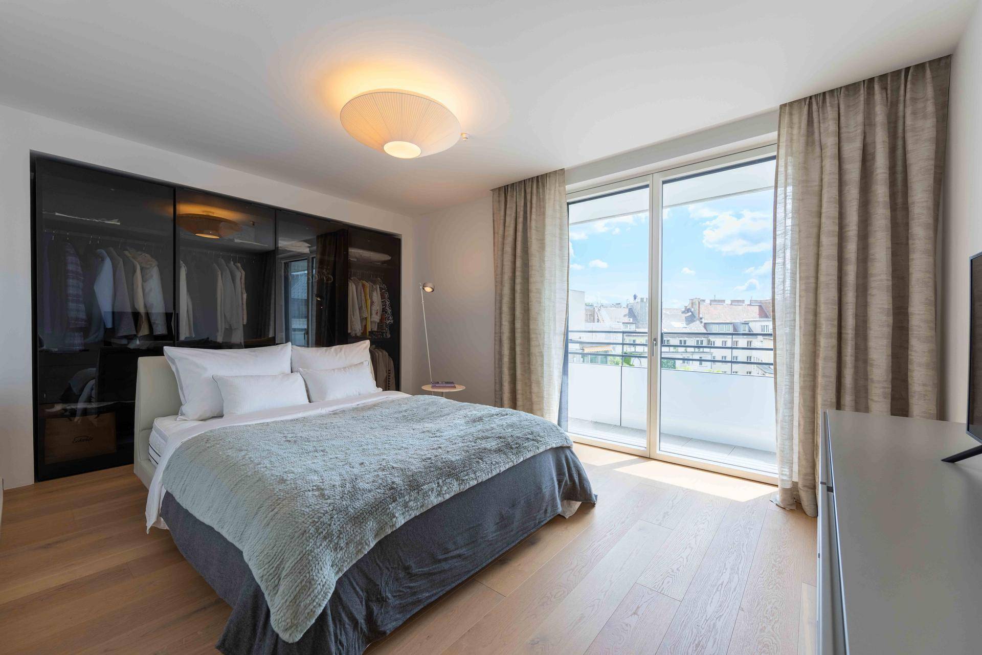 Helles Schlafzimmer mit großem Bett, Einbauschränken und Zugang zum Balkon.