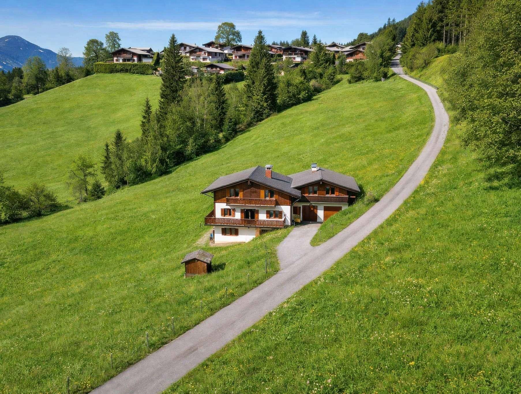 Luftaufnahme eines traditionellen Hauses auf einem grünen Hügel mit Zufahrt und umliegender Natur.