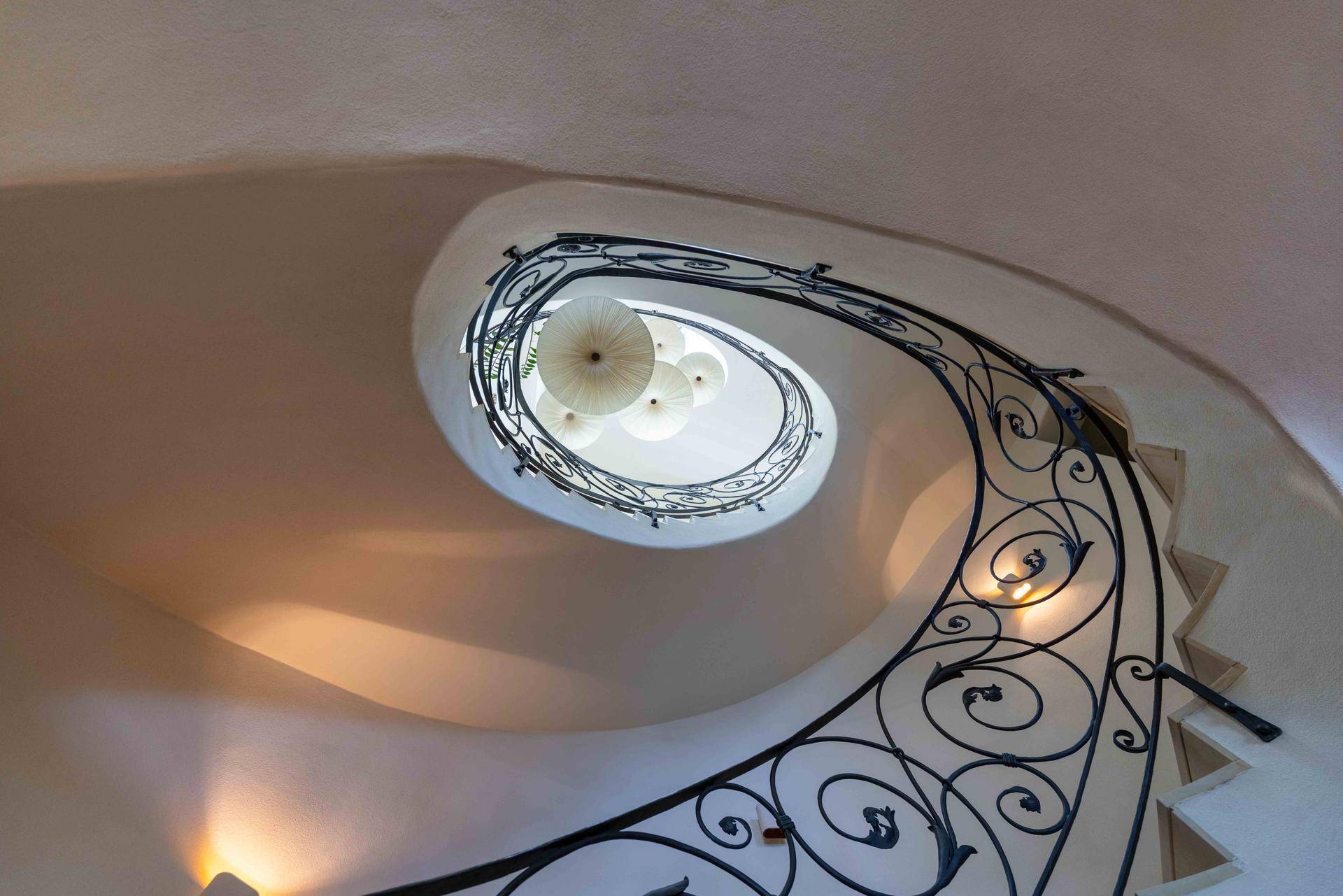 Elegante Wendeltreppe mit kunstvollem schmiedeeisernem Geländer und Deckenleuchte.