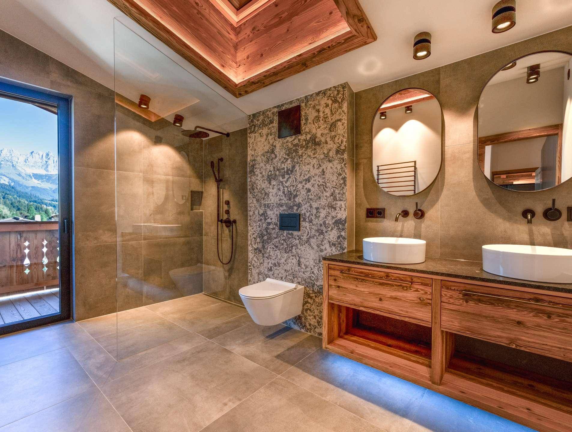Modernes Badezimmer mit Doppelwaschbecken, begehbarer Dusche und Zugang zu einem Balkon mit Bergblick.