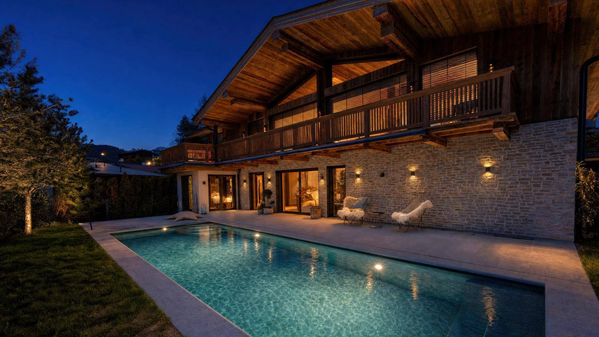 Luxuriöses Chalet mit beleuchtetem Außenpool und gepflegtem Garten in der Abenddämmerung.