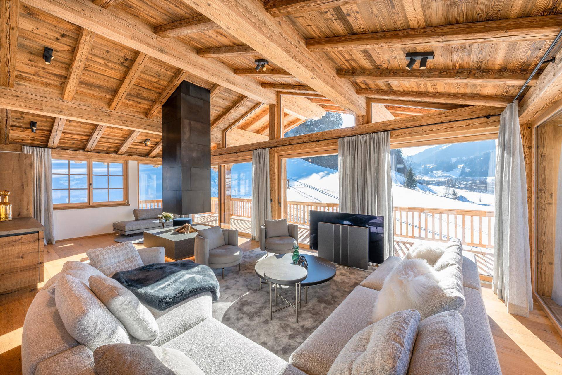 Helles Wohnzimmer im Chalet-Stil mit Holzbalken, Kamin und Panoramablick auf die verschneite Berglandschaft.
