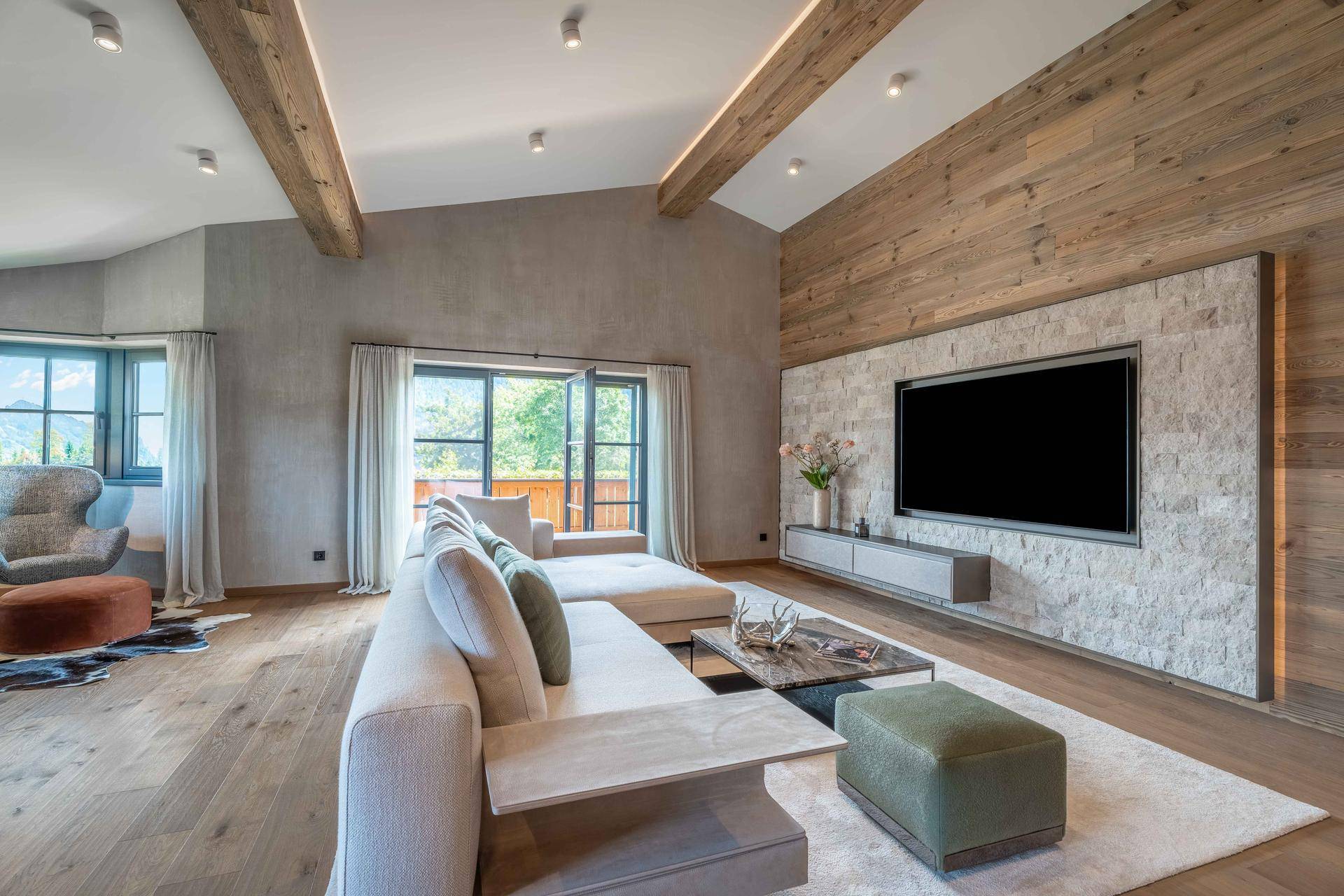 Geräumiges Wohnzimmer im alpinen Stil mit Holzbalken, Steinwand und Bergblick.