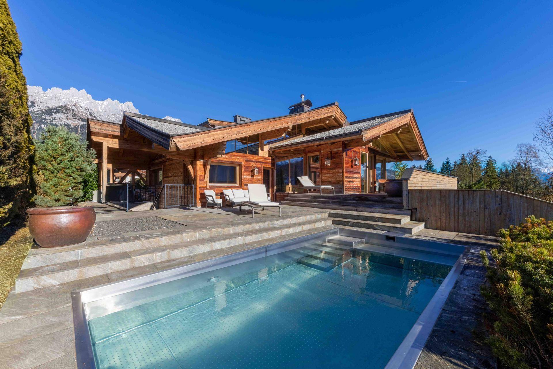 Sonnige Terrasse mit modernem Pool und Liegeflächen vor beeindruckender Bergkulisse.