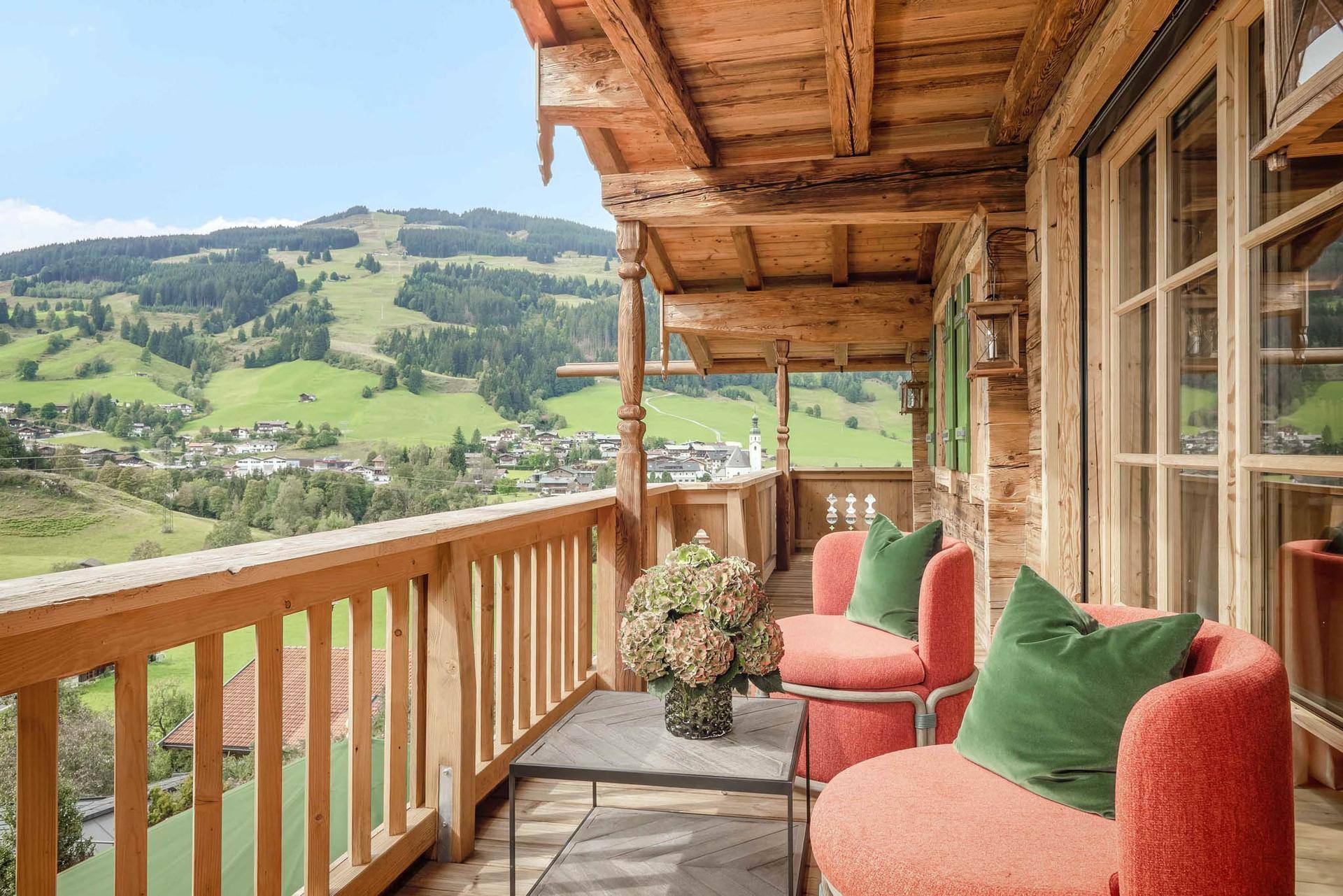 Geräumiger Holzbalkon mit Sitzgelegenheiten und weitem Blick über die grüne Berglandschaft.