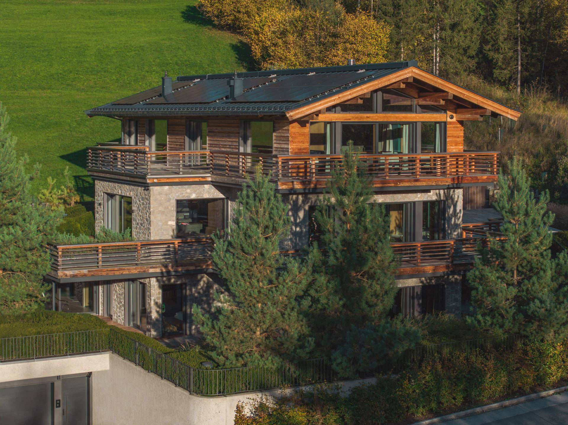 Exklusives Chalet mit moderner Holz- und Steinfassade, mehreren Balkonen und umgeben von Nadelbäumen.